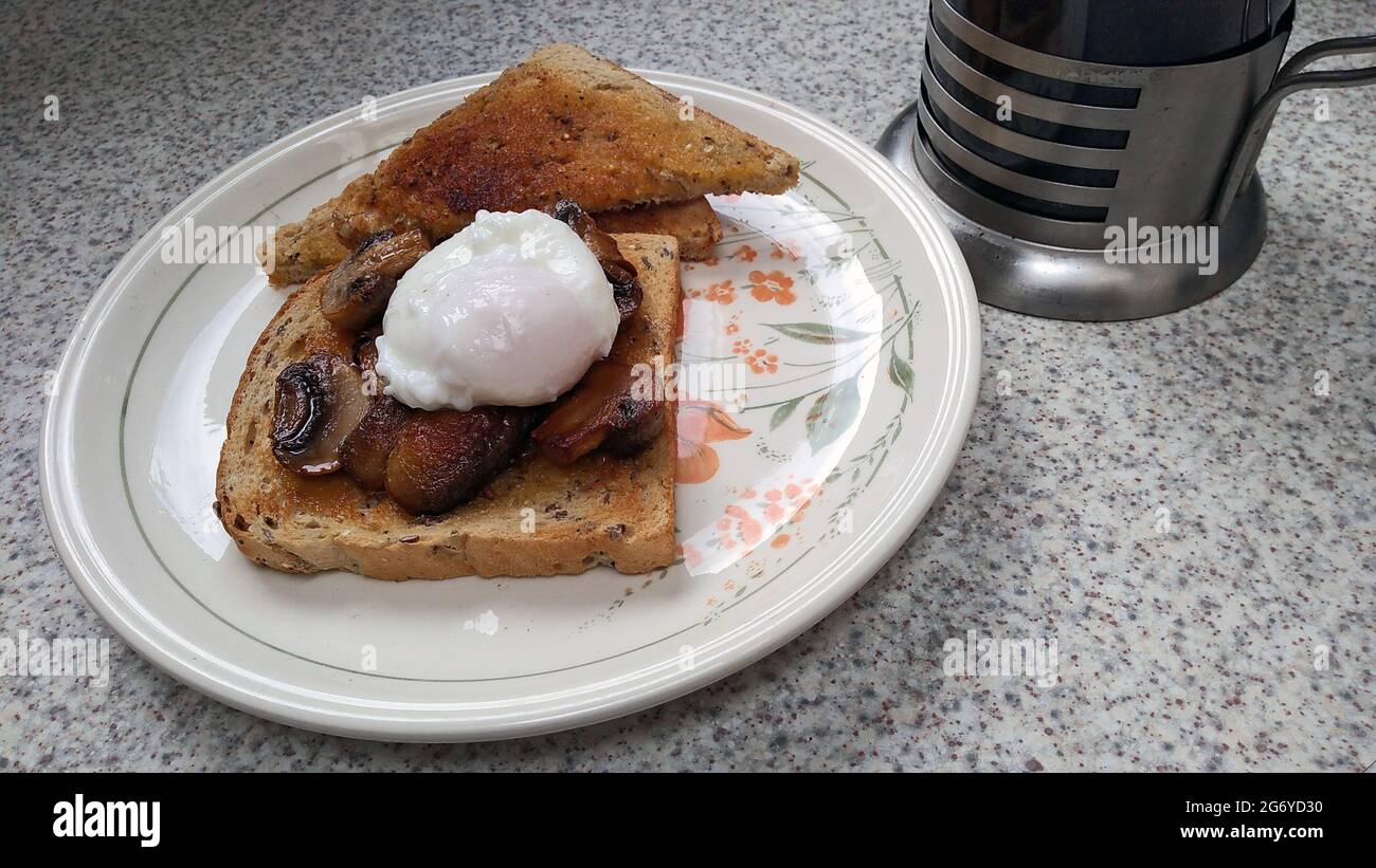 NEWTON le WILLOWS. MERSEYSIDE. ENGLAND. 06-20-21. A poached egg served on toast with mushrooms, alongside a caffetier of ground coffee. Stock Photo