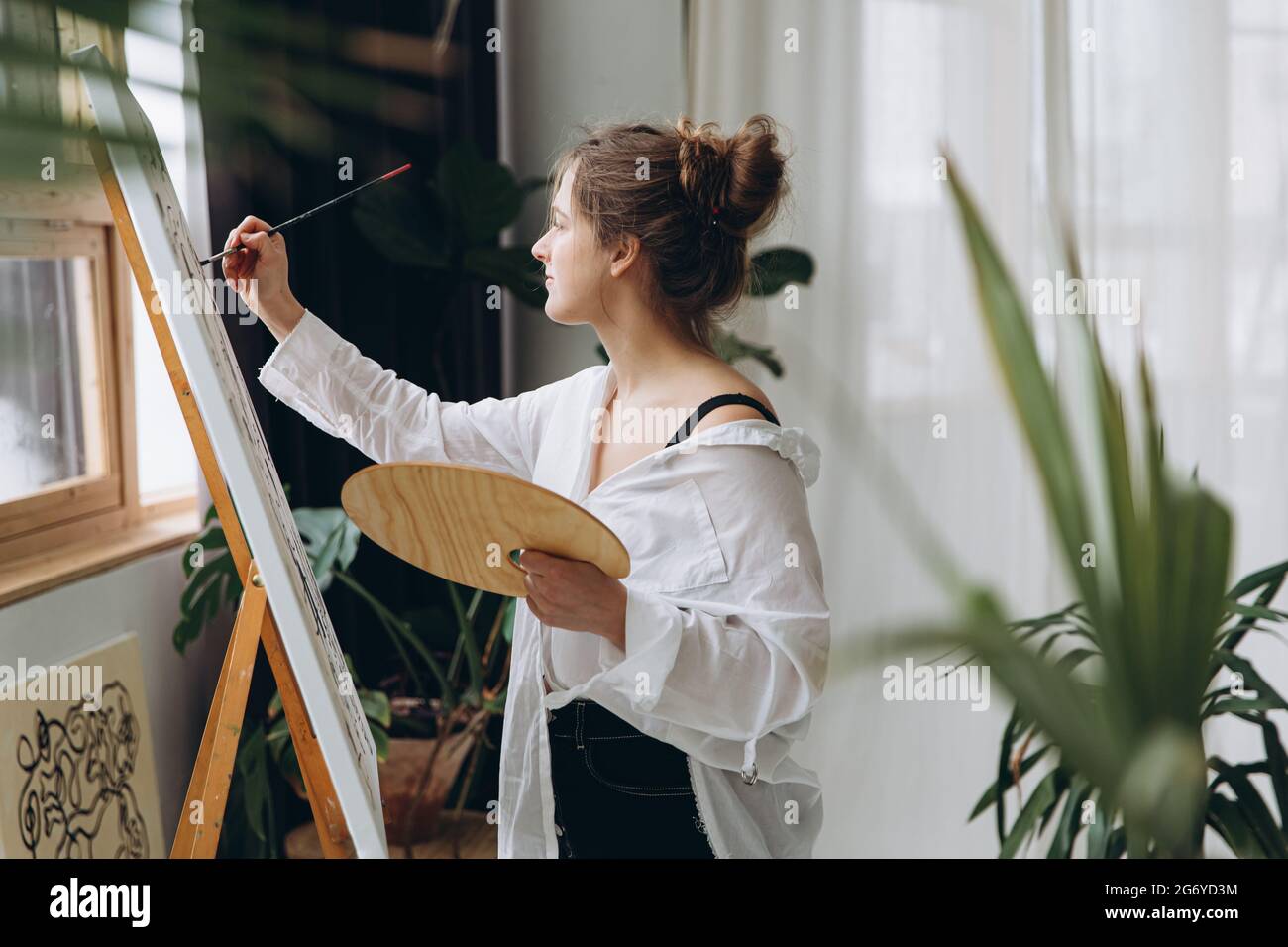 Side view of young woman painting on canvas with brush Stock Photo