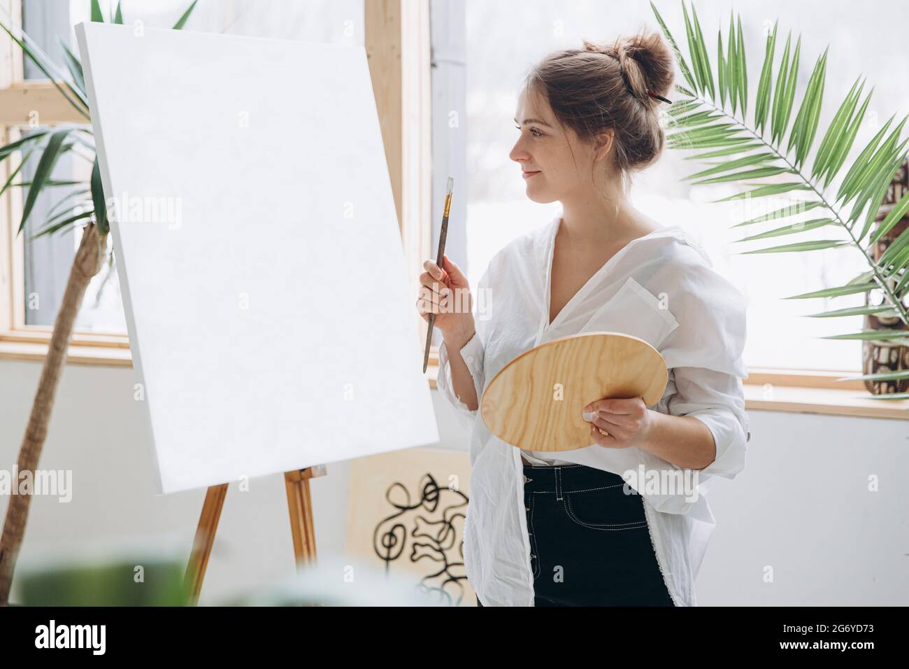 Positive woman holding paint brush and wooden art palette Stock Photo