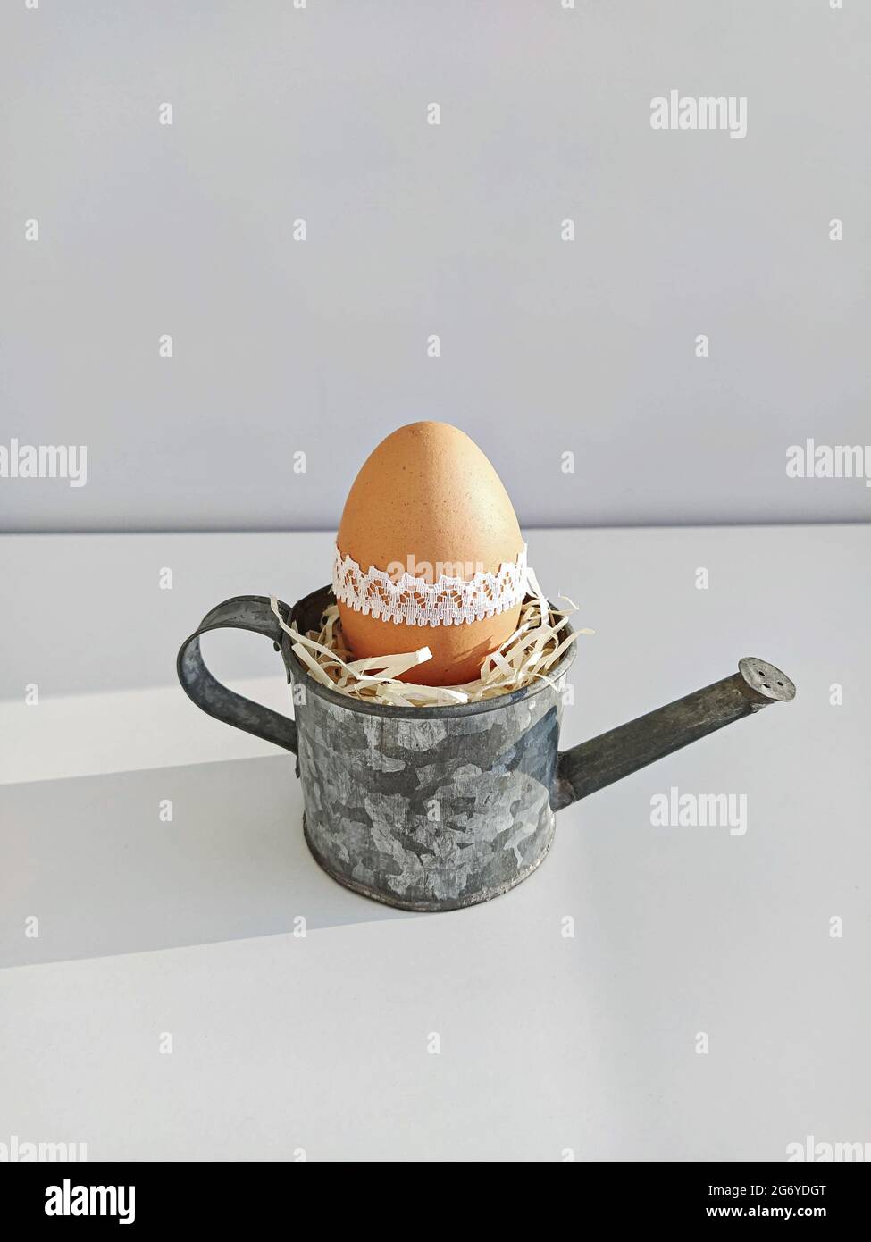 Easter egg in small decorative steel watering can on light background. Easter DIY table decoration Stock Photo