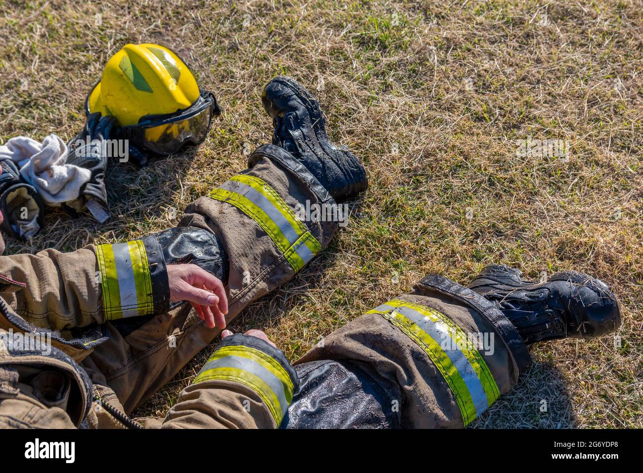 Firefighter's yellow helmet set on the ground outside with firemen resting outside on a sunny day Stock Photo