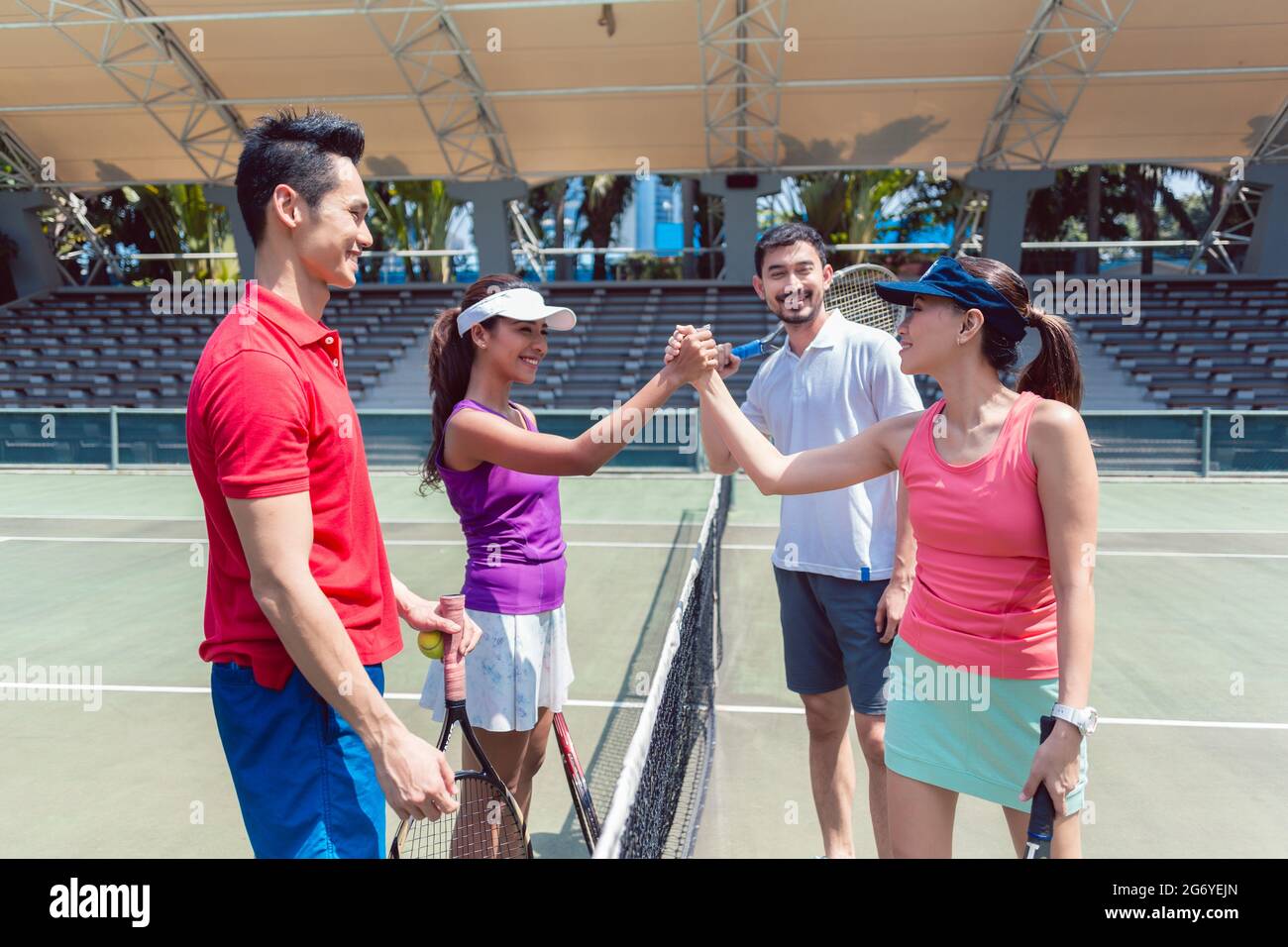 Four young and competitive tennis players putting hands together above
