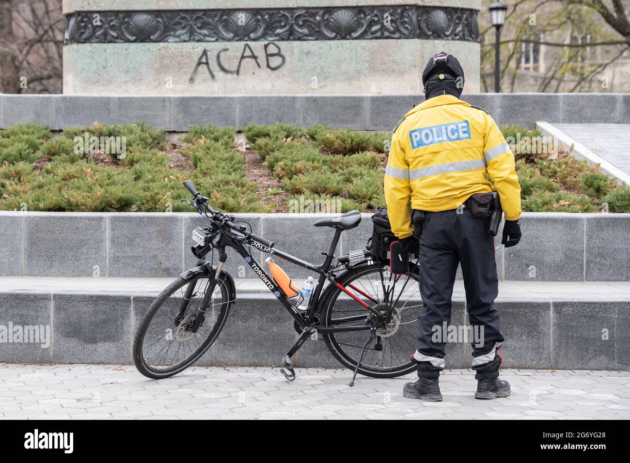 A police officer stands in front of anti-police ACAB ('All Cops Are Bastards') graffiti in Queen's Park, Toronto. Stock Photo