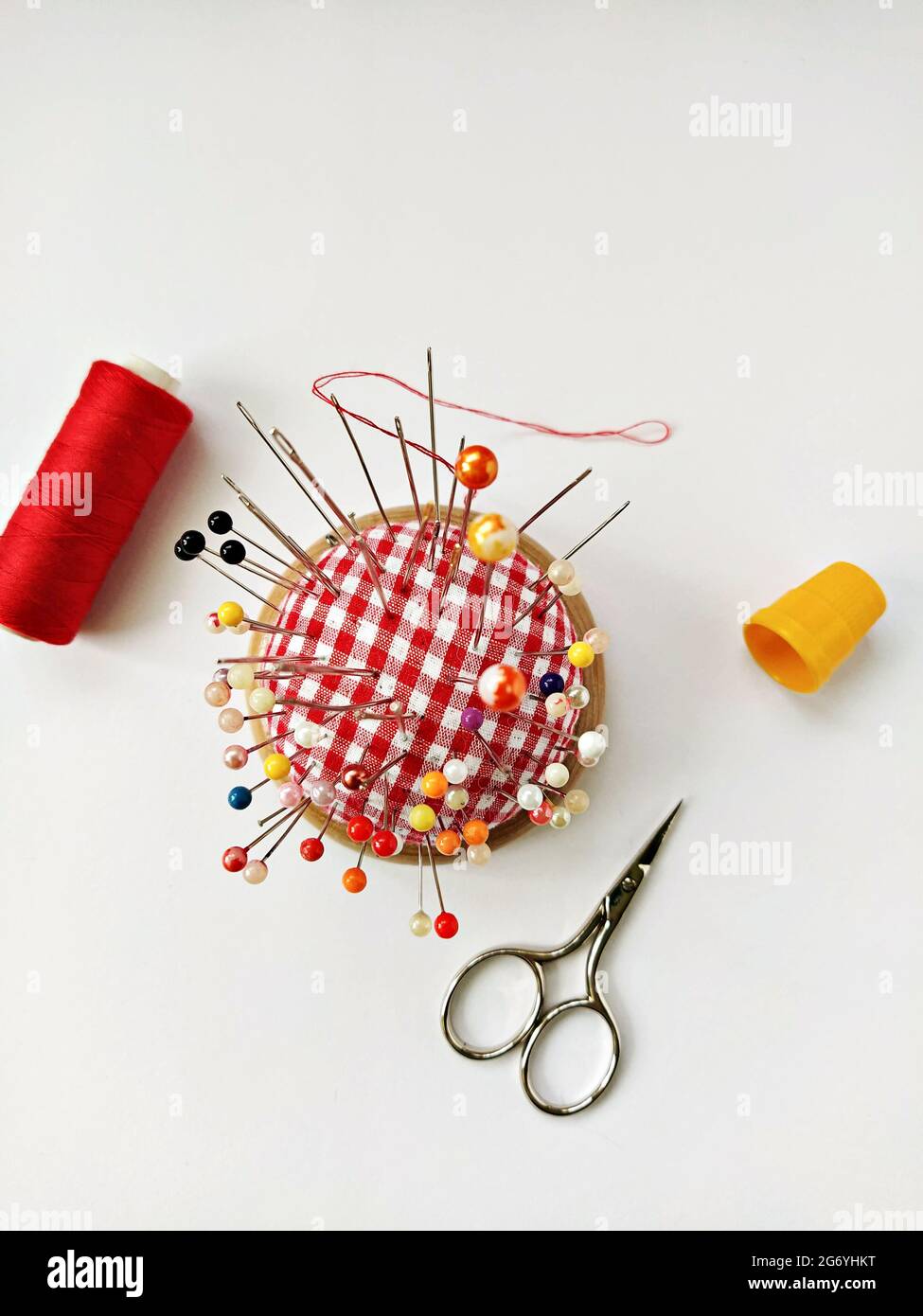 Round pin cushion with lot of pins, yellow thimble, spool of thread and scissors. Sewing accessories flat lay on white background Stock Photo