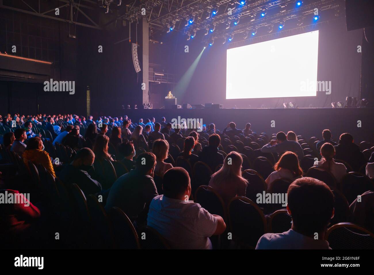 Audience sitting in front of stage with screen Stock Photo Alamy