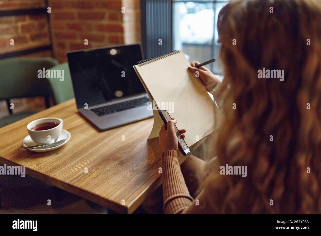 Woman using smartphone and writing in notebook Stock Photo