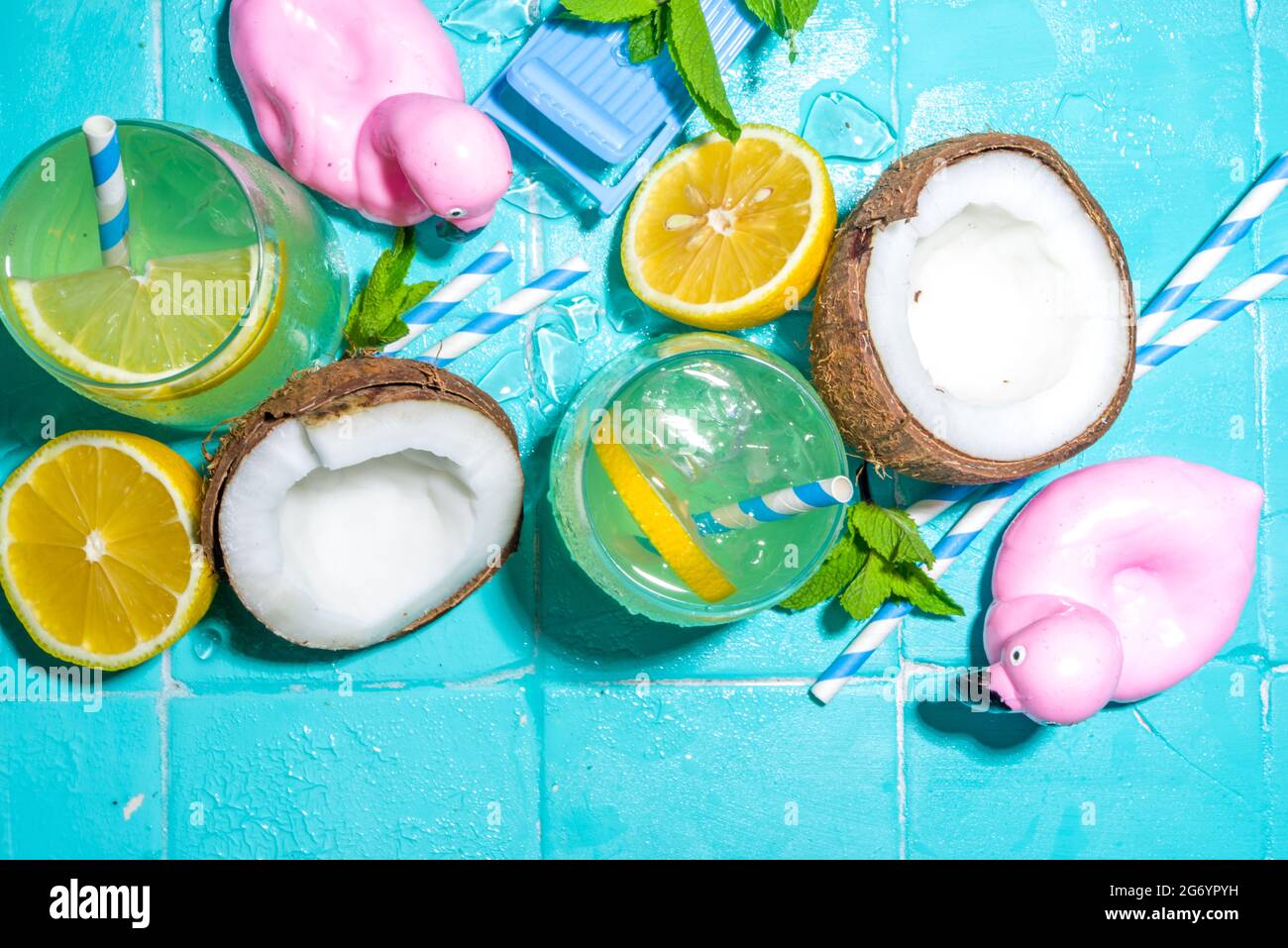 Bright sunny summer vacation. Lemonade drink on wet blue pool tiles background, with beach holiday accessories, flamingo lifebuoys, lemons, coconuts, Stock Photo