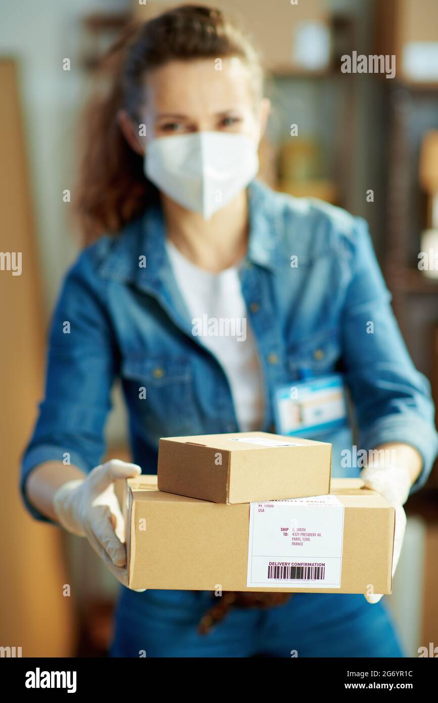 Delivery business. Closeup on female in jeans with ffp2 mask giving parcel in the warehouse. Stock Photo