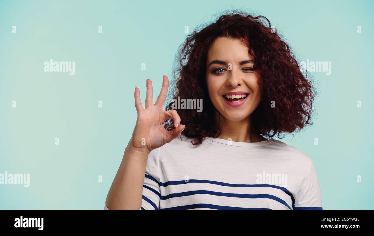 Winking Signl positive young woman in striped long sleeve shirt showing ok sign and ...