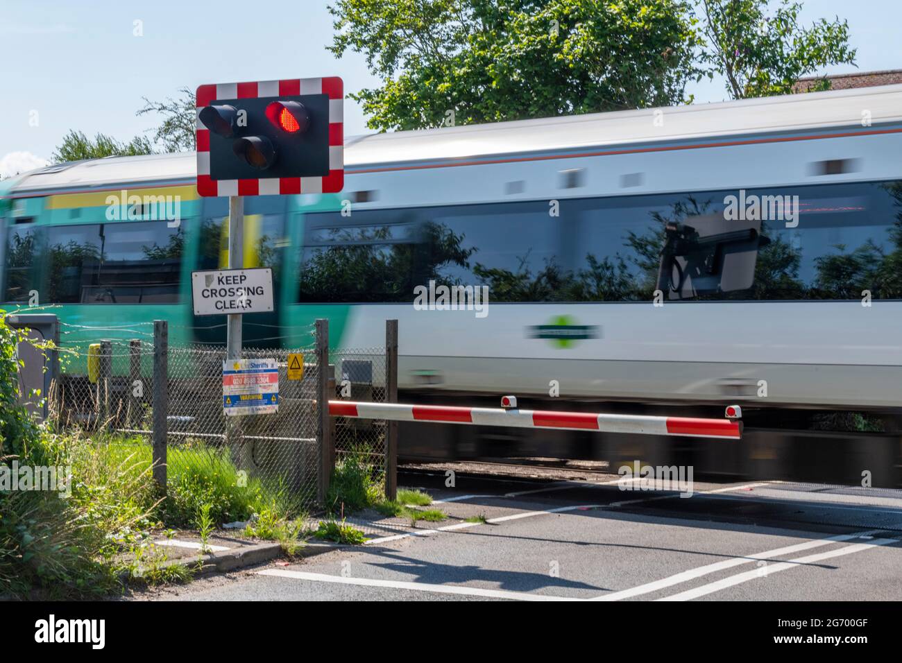 a southern train going over a level crossing automatic half barriers with the barrier down closing the road to traffic Stock Photo