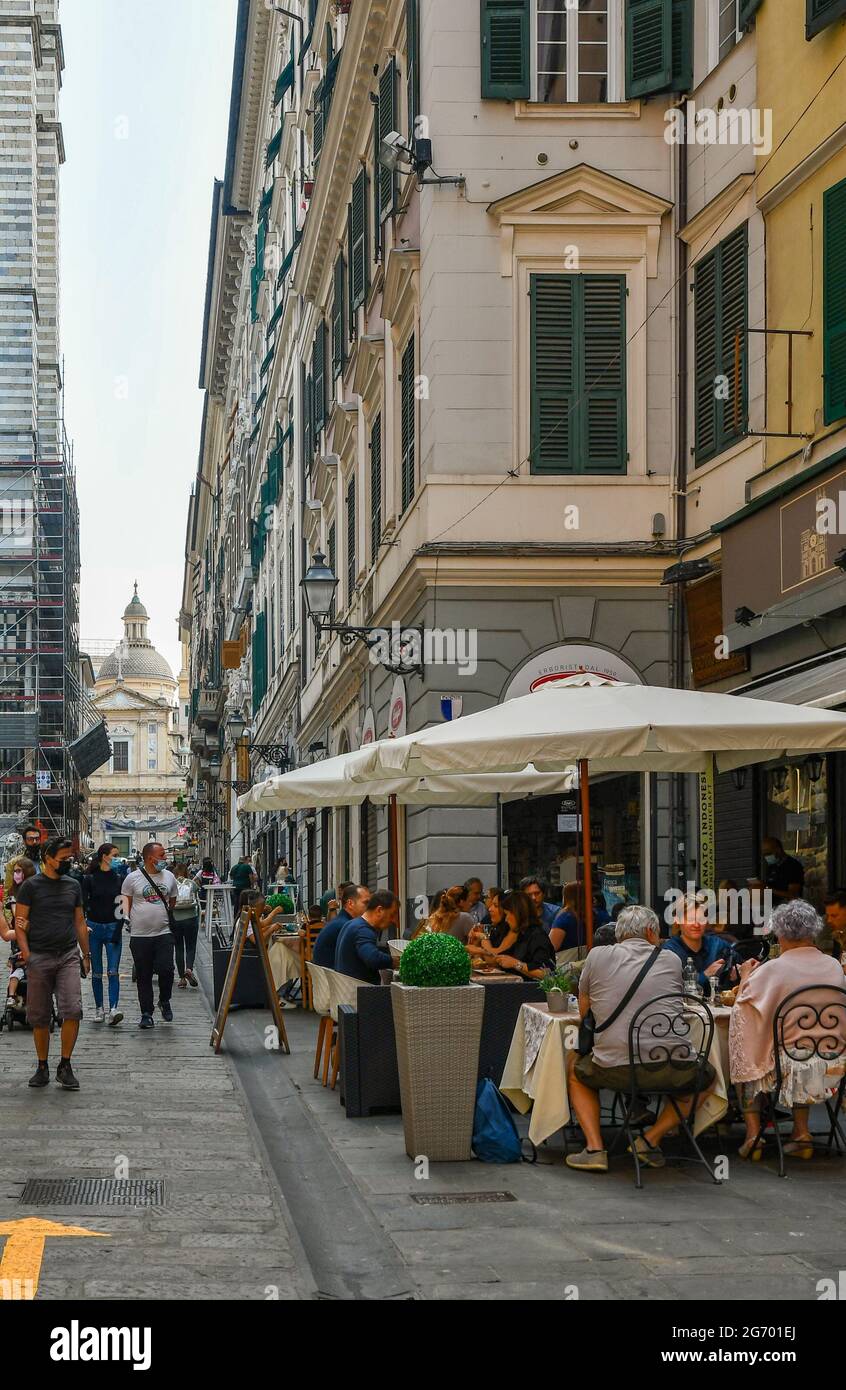 Via San Lorenzo, one of the main street, with people having lunch in an outdoor restaurant and the Church of Jesus in the background, Genoa, Italy Stock Photo