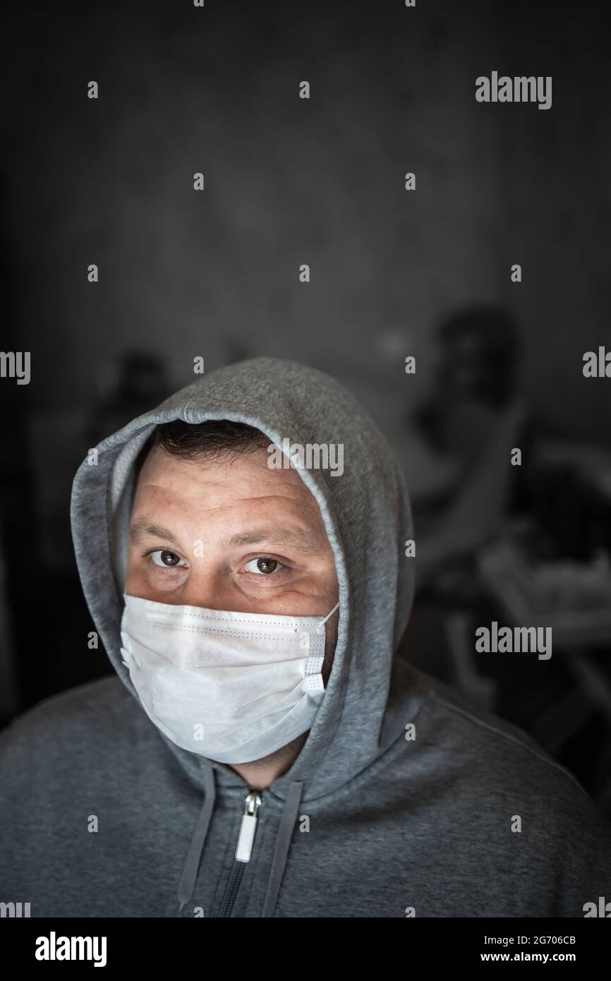 Young adult male with a gray hood in a medical mask. Restless serious look straight. Dark gray background. Selective focus. Concept, prevention of vir Stock Photo