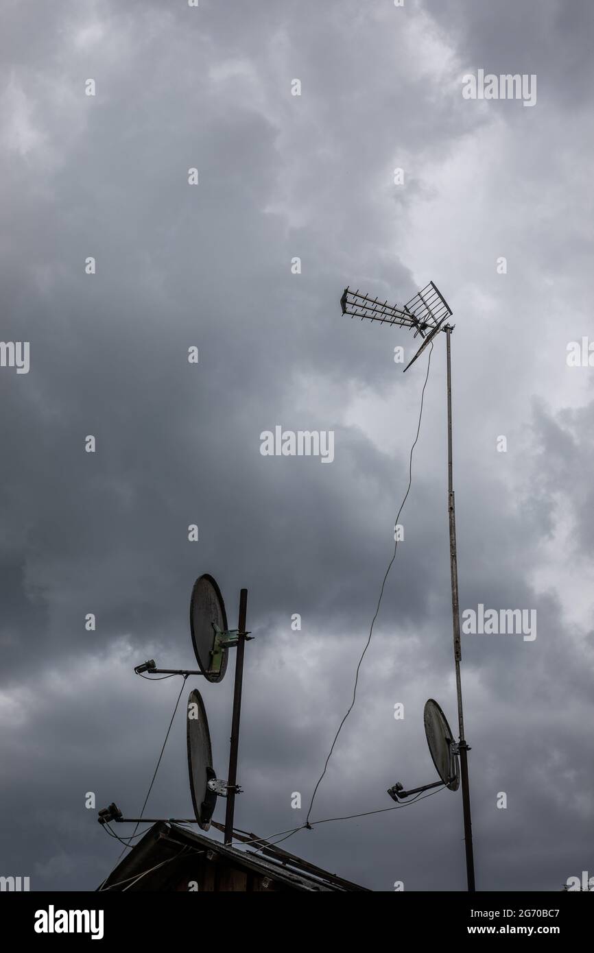 dark, grey, cloudy, sky before the storm and rooftop with metal antenna and satellite dishes Stock Photo