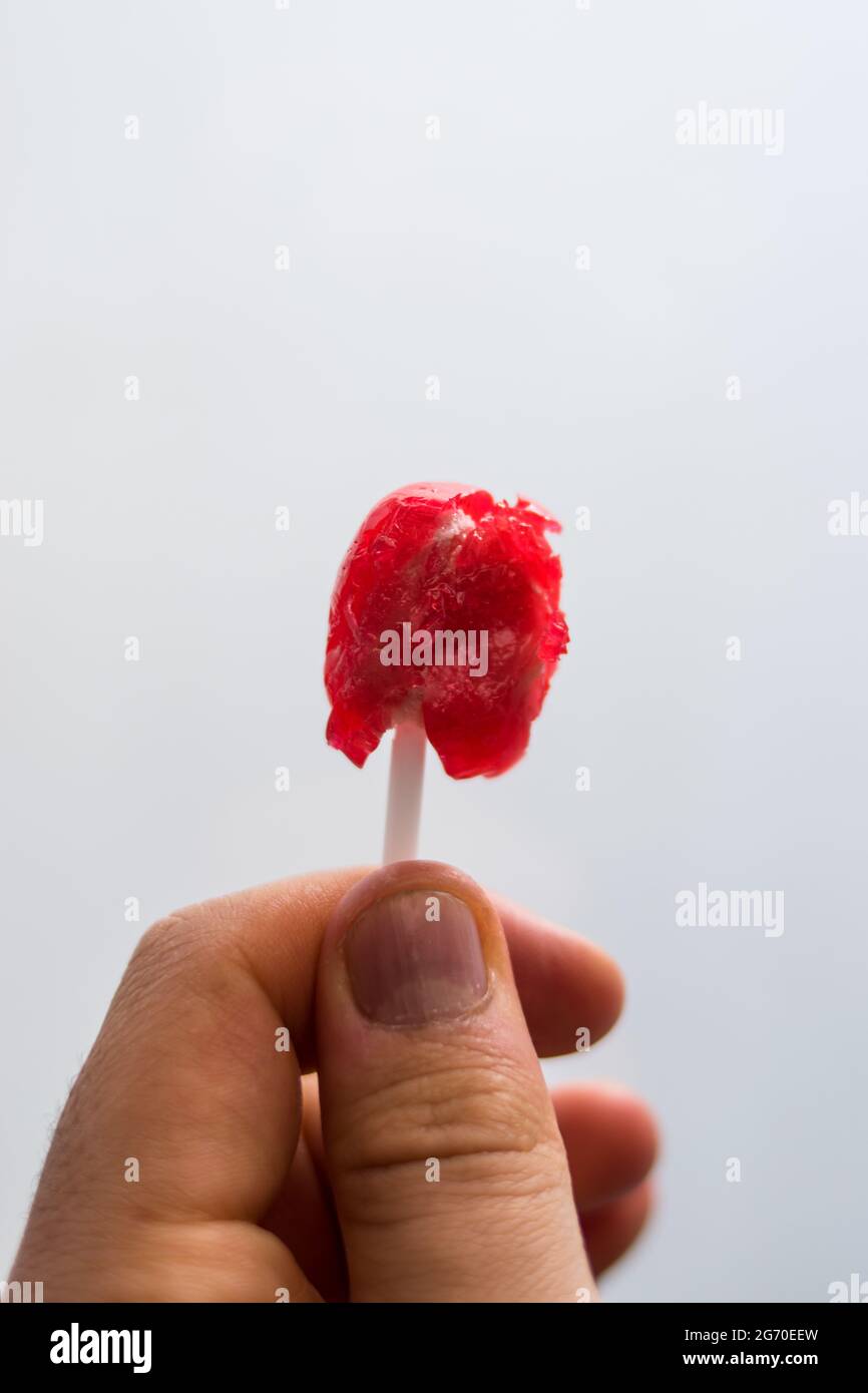 Hand holding a red bite lollipop with a white background Stock Photo