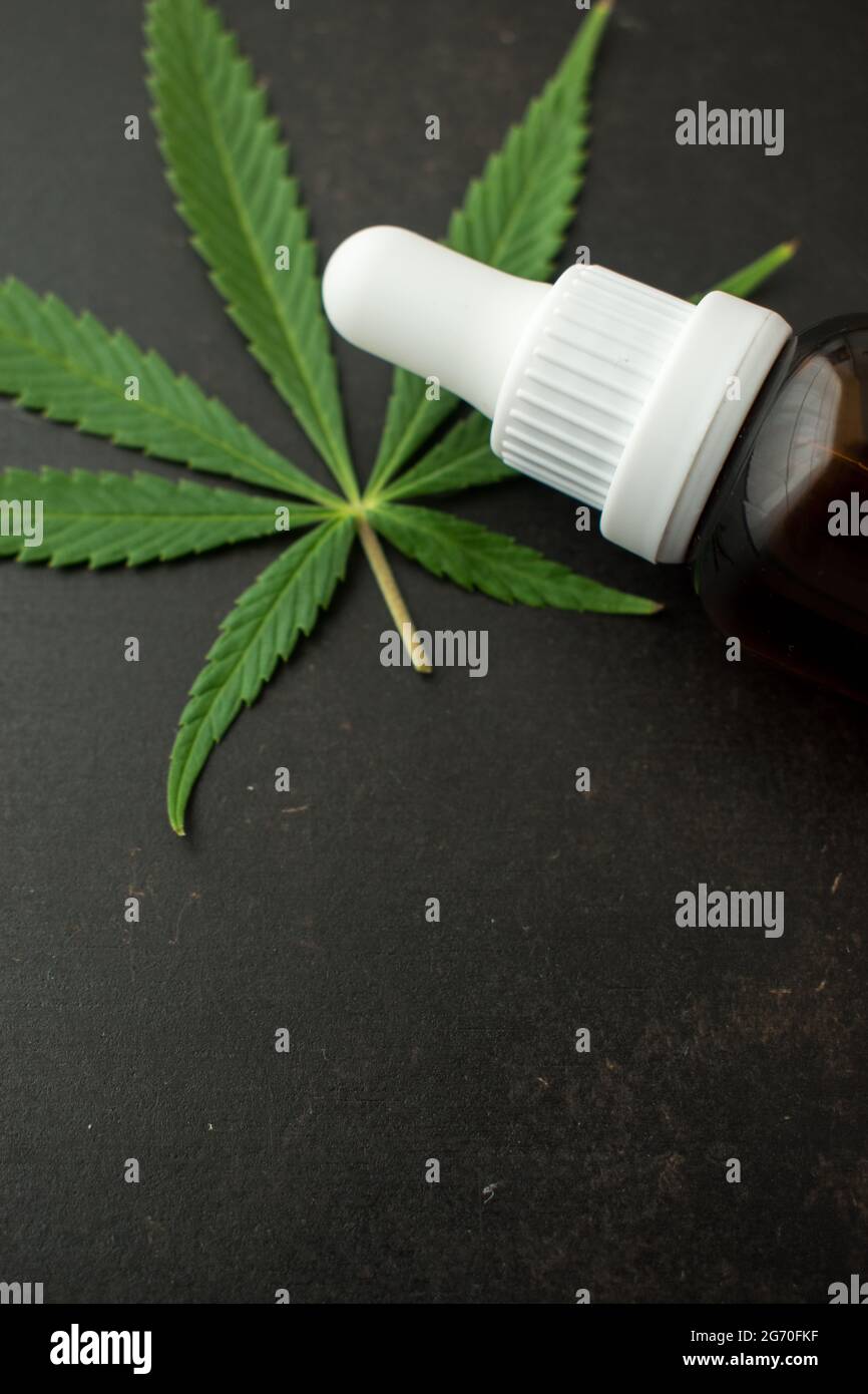 Glass brown bottle of dropper with some cannabis leaves on a black wooden table with copy space Stock Photo