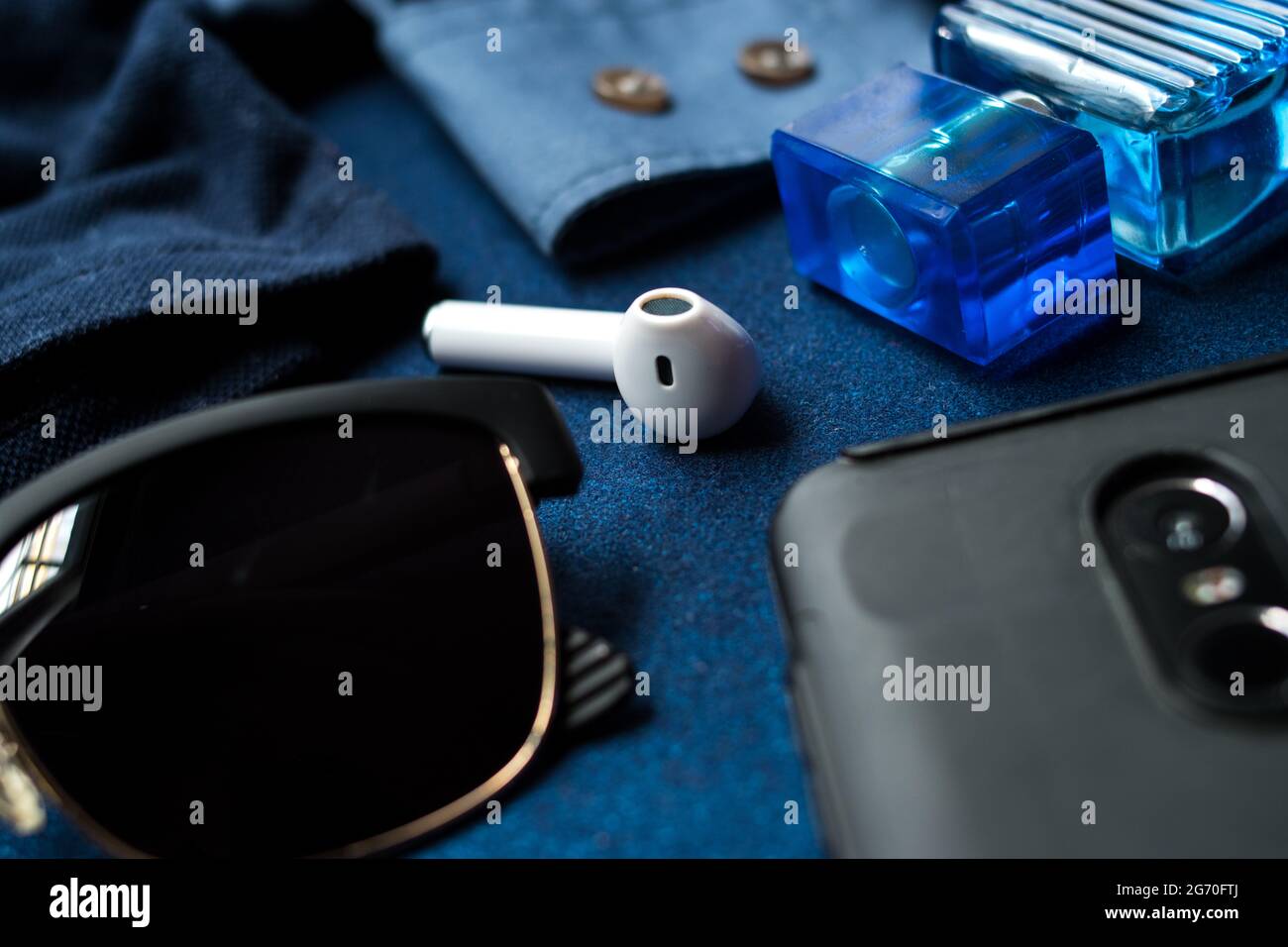 Some sunglasses, black cellphone, wireless earphone and glass lotion bottle on a blue textured desk Stock Photo