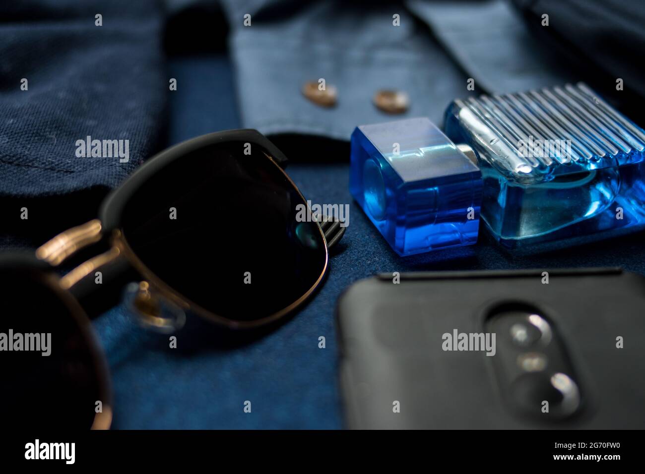 Some sunglasses, black cellphone, and glass lotion bottle on a blue textured desk Stock Photo