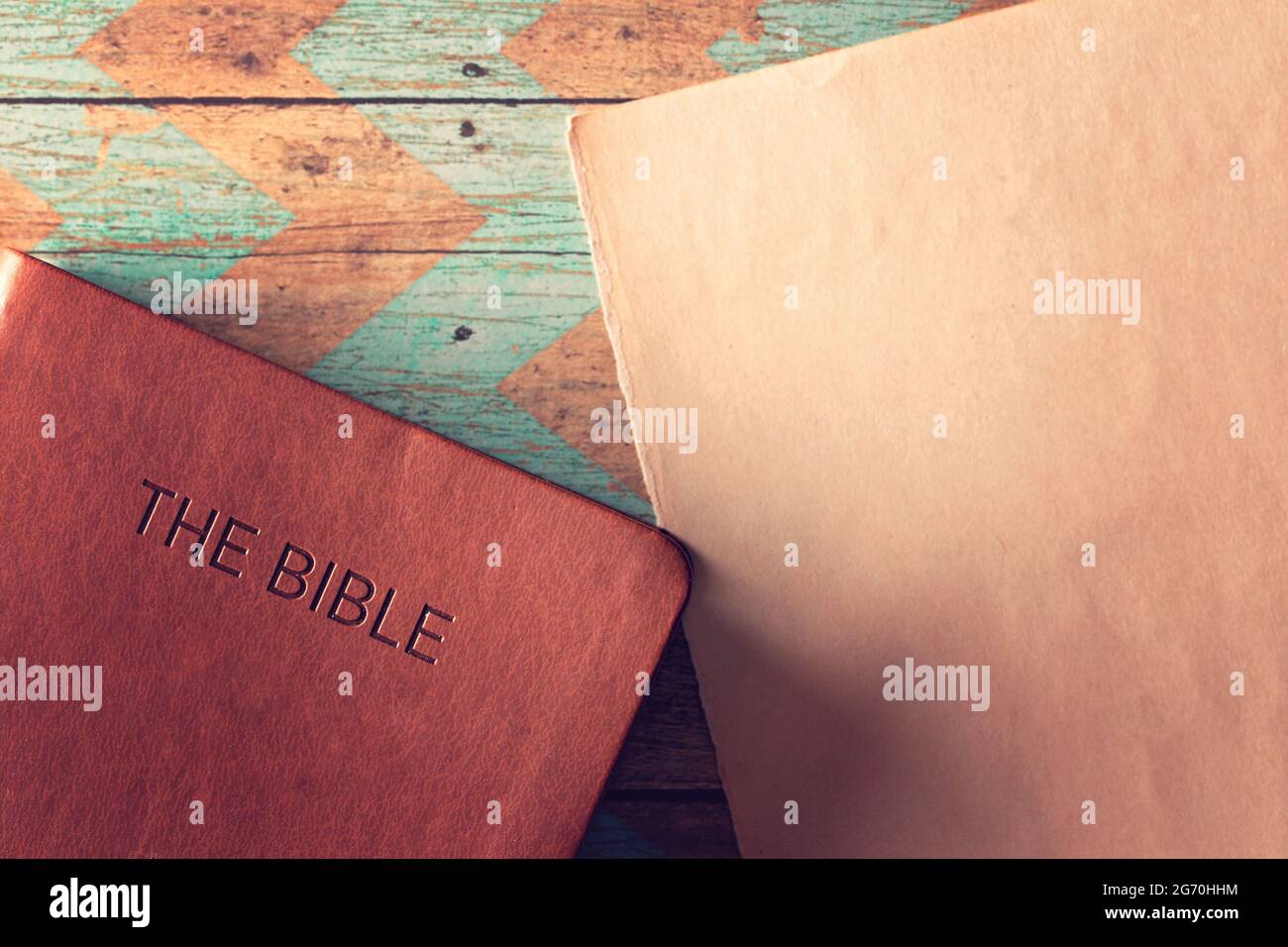 The Holy Bible on a Rustic Wooden Table with a Blank Piece of Antique Paper for Adding Text Stock Photo