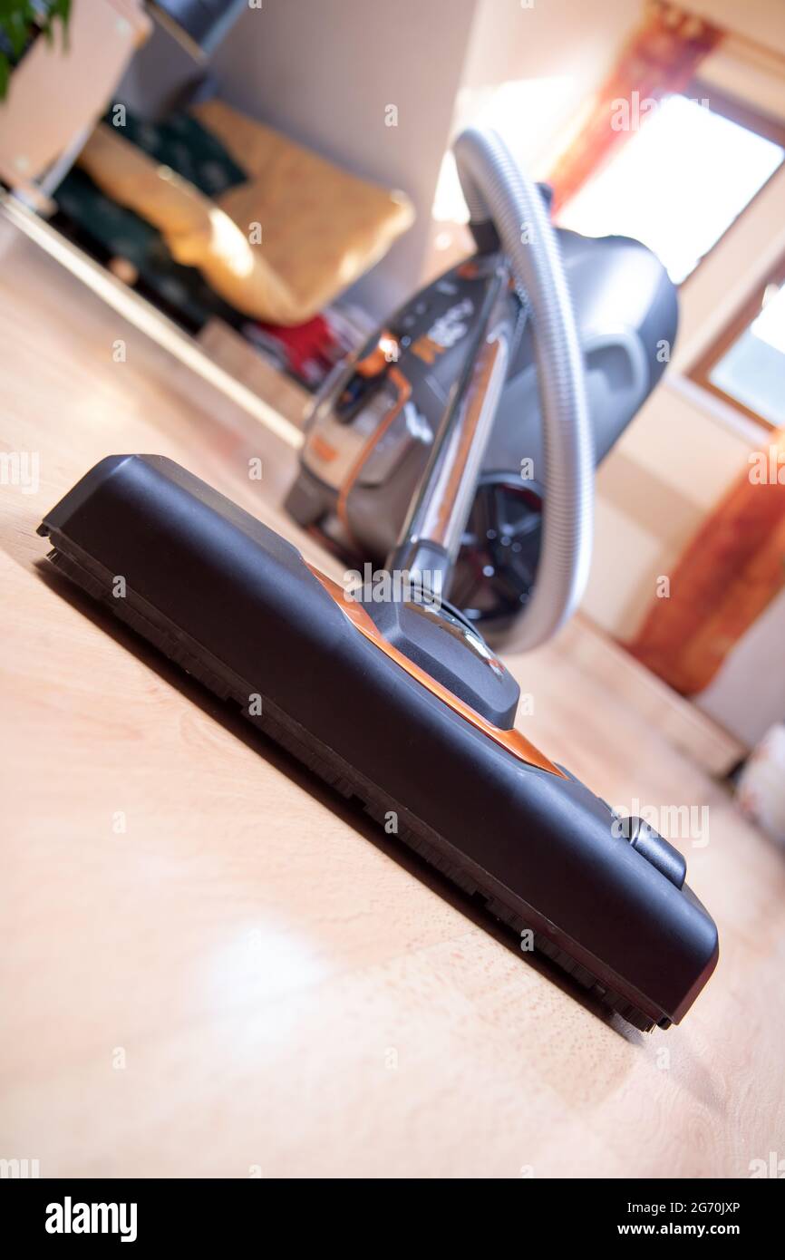 The Vacuum Cleaner on a laminate floor at room with windows on background. Cleaning the wooden floors with hoover, close up view. Stock Photo