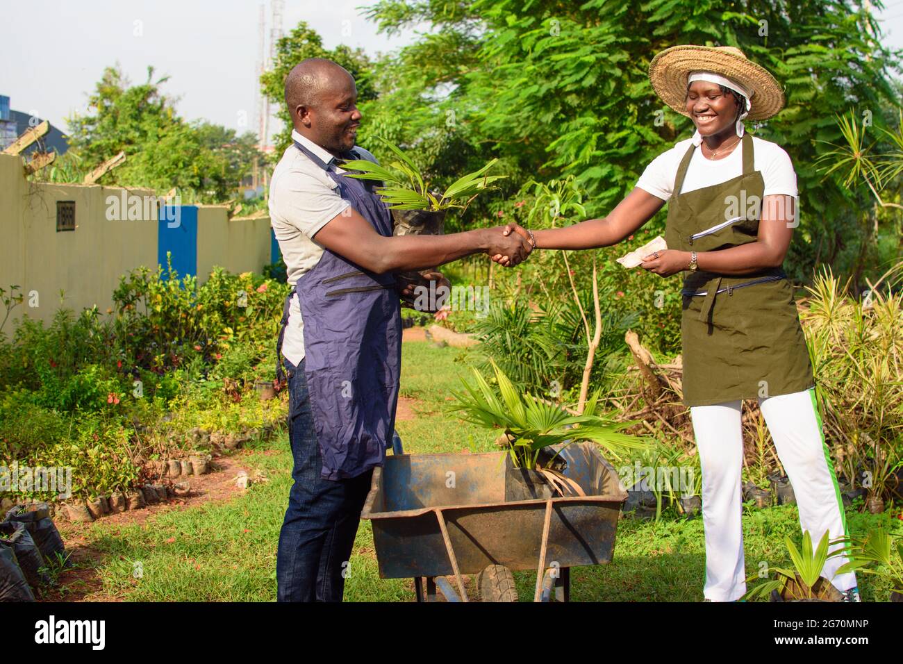 African female and male gardener, florist or horticulturist working together in a garden filled with variety of colorful flowers and plants, exchangin Stock Photo