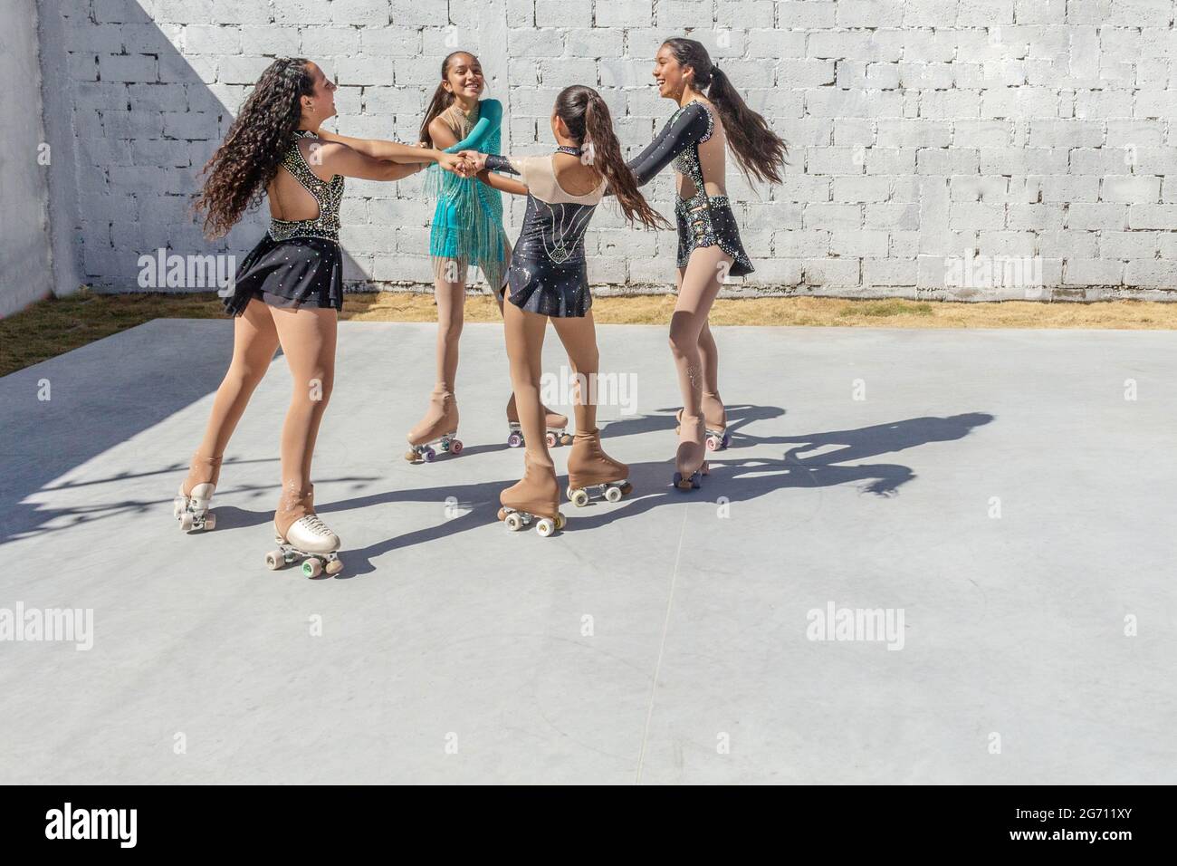 Four latina teenage girls dancing on four-wheel skates making a circle or playing a round outdoors on a sunny morning Stock Photo