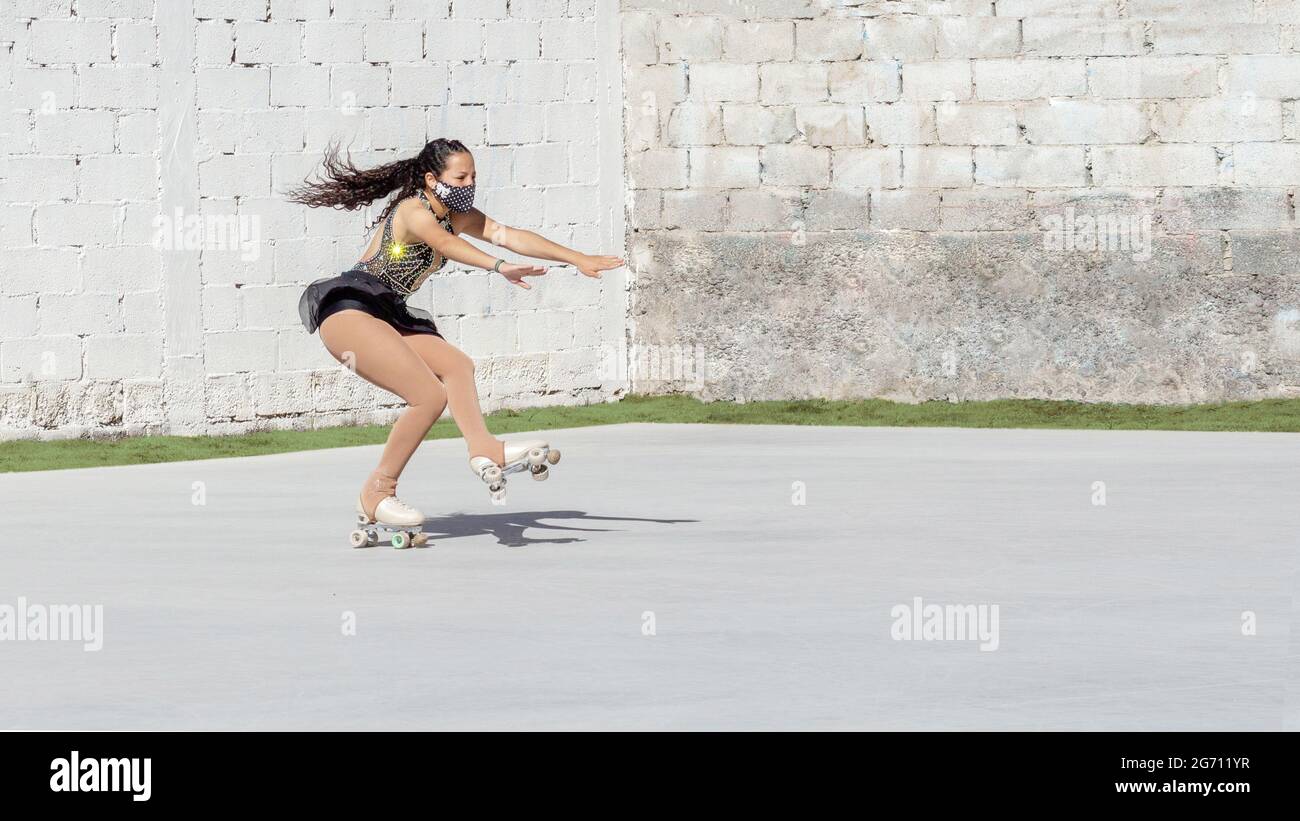 Latin teenager with mask, performing figure skating on roller, falling from an axel jump outdoors Stock Photo