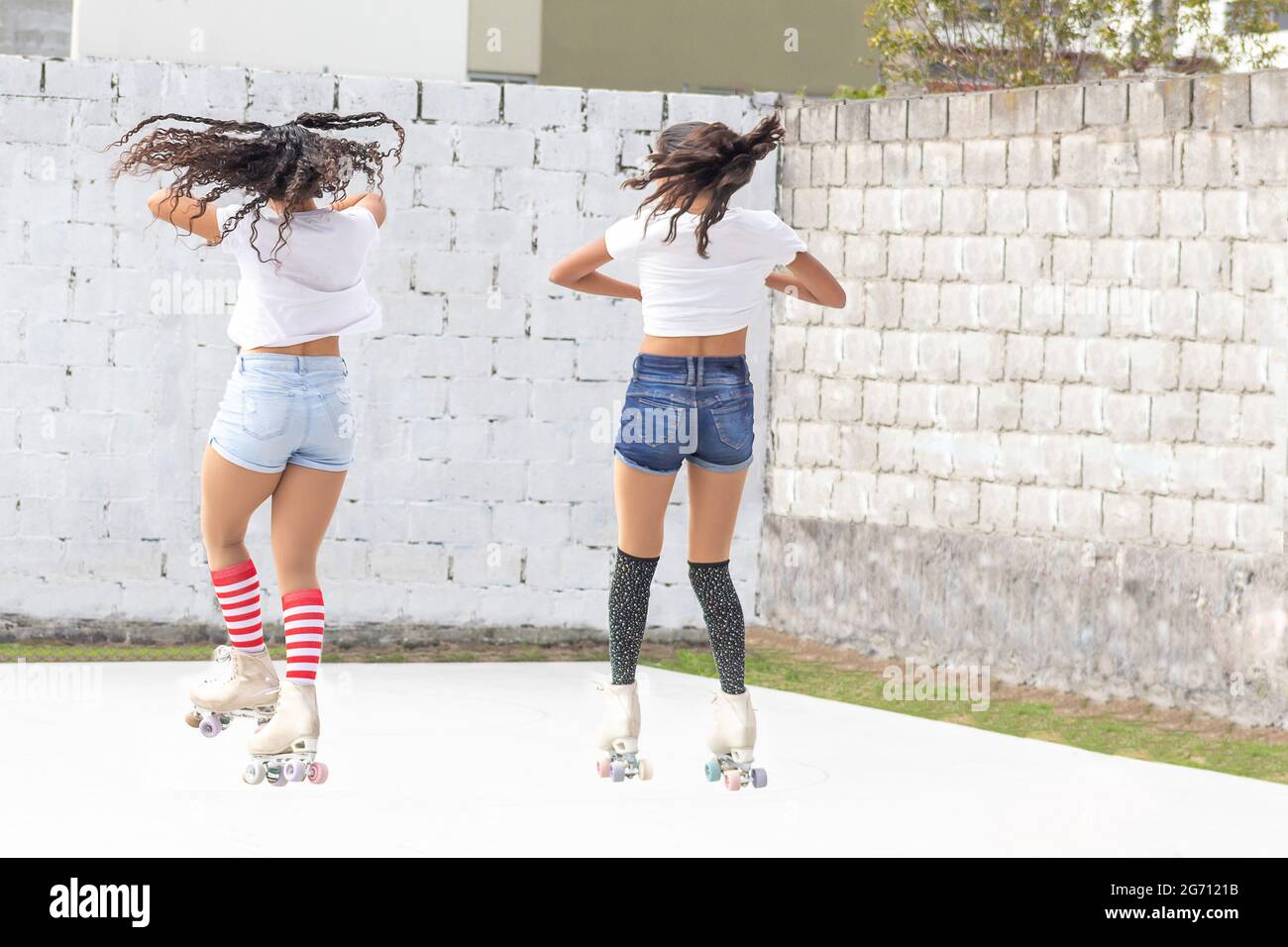 Two teenage girls jumping and spinning on roller skates on a summer morning Stock Photo