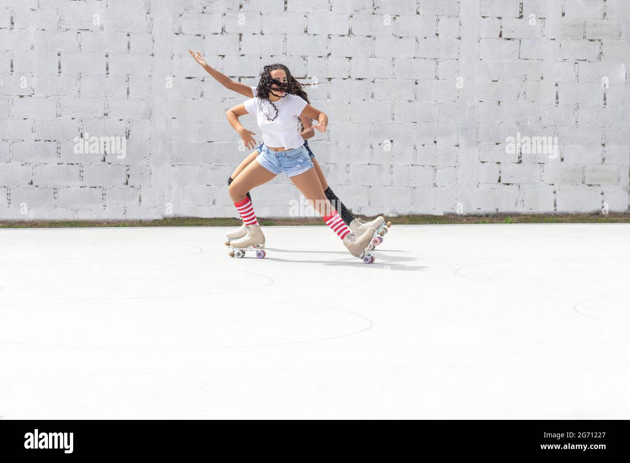 Two teenage Latin girls dressed in white t-shirts and shorts dance fun on four-roller skates Stock Photo