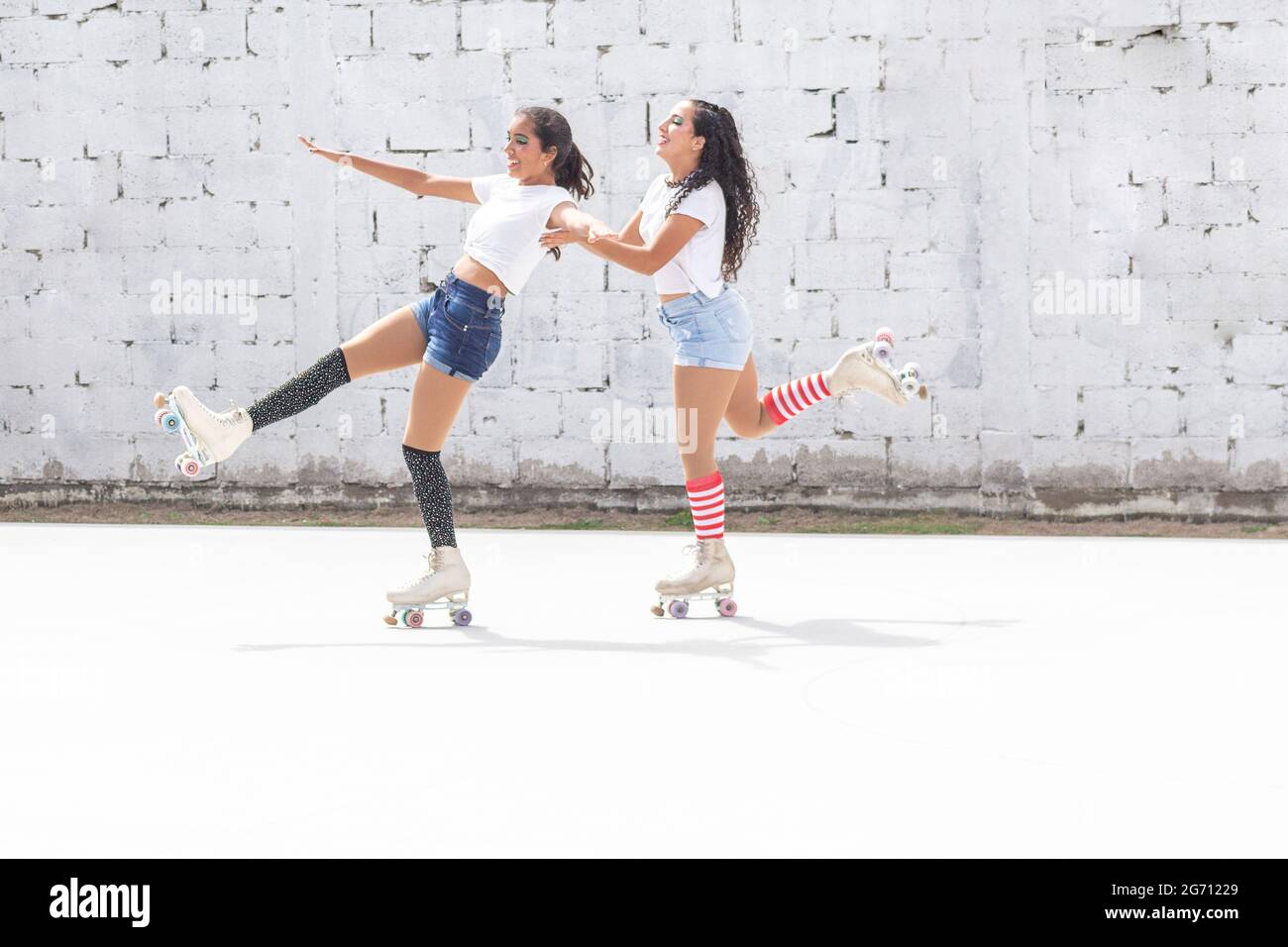 Two friends in shorts, white t-shirt and long socks skate fun on roller skates on a summer morning Stock Photo