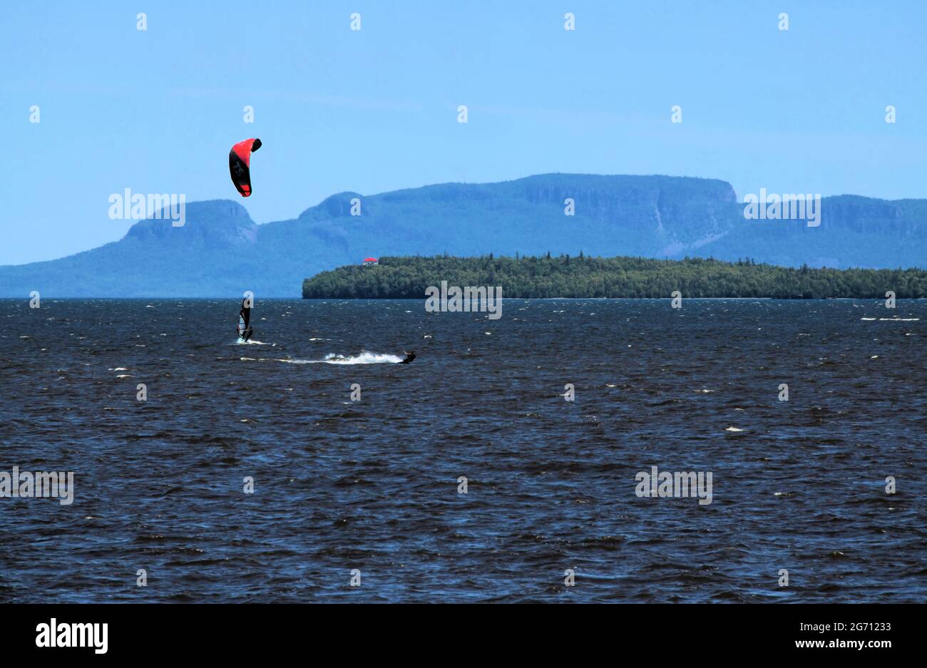 In the Bay at Mission Marsh two men are windsurfing and parasailing in Lake Superior, with the Sleeping Giant and one Welcome Island in the background. Stock Photo