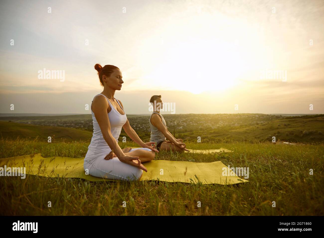Couple sitting in lotus position with eyes closed, meditating and practicing yoga on nature together Stock Photo