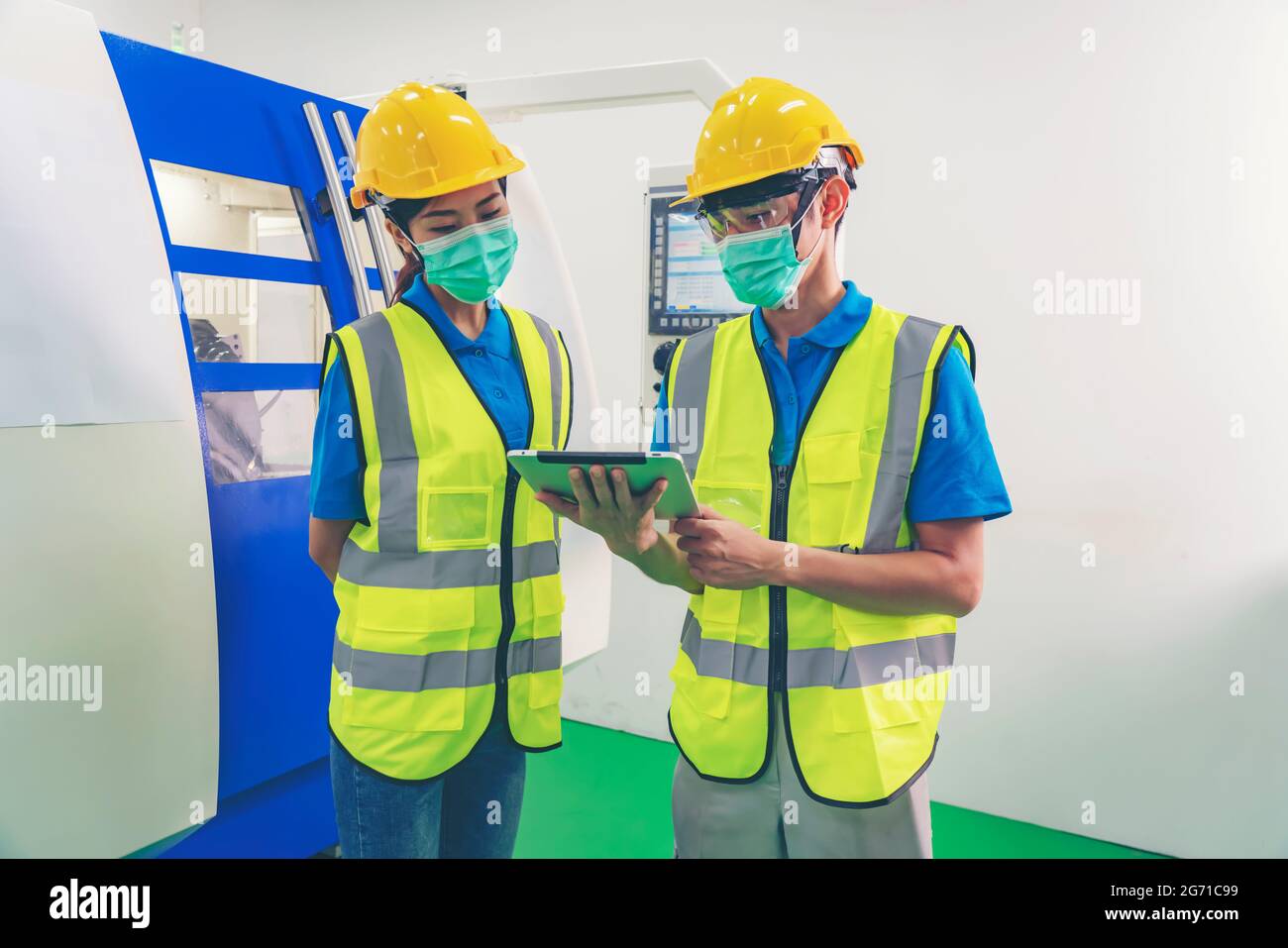 Male industrial engineer or technician worker wear face mask with safety and hard helmet training trainee assistant using control machine operating co Stock Photo