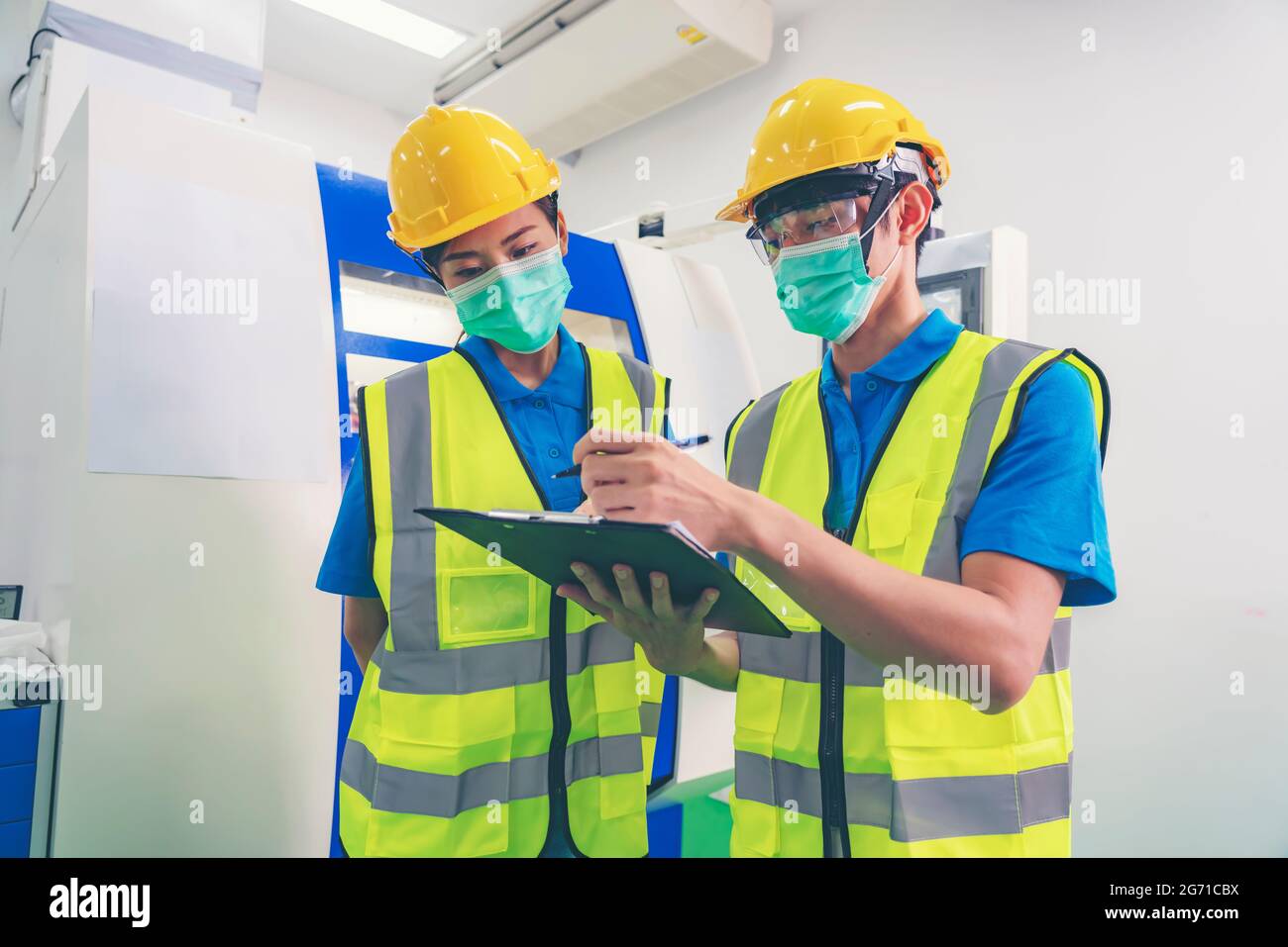 Male industrial engineer or technician worker wear face mask with safety and hard helmet training trainee assistant using control machine operating co Stock Photo