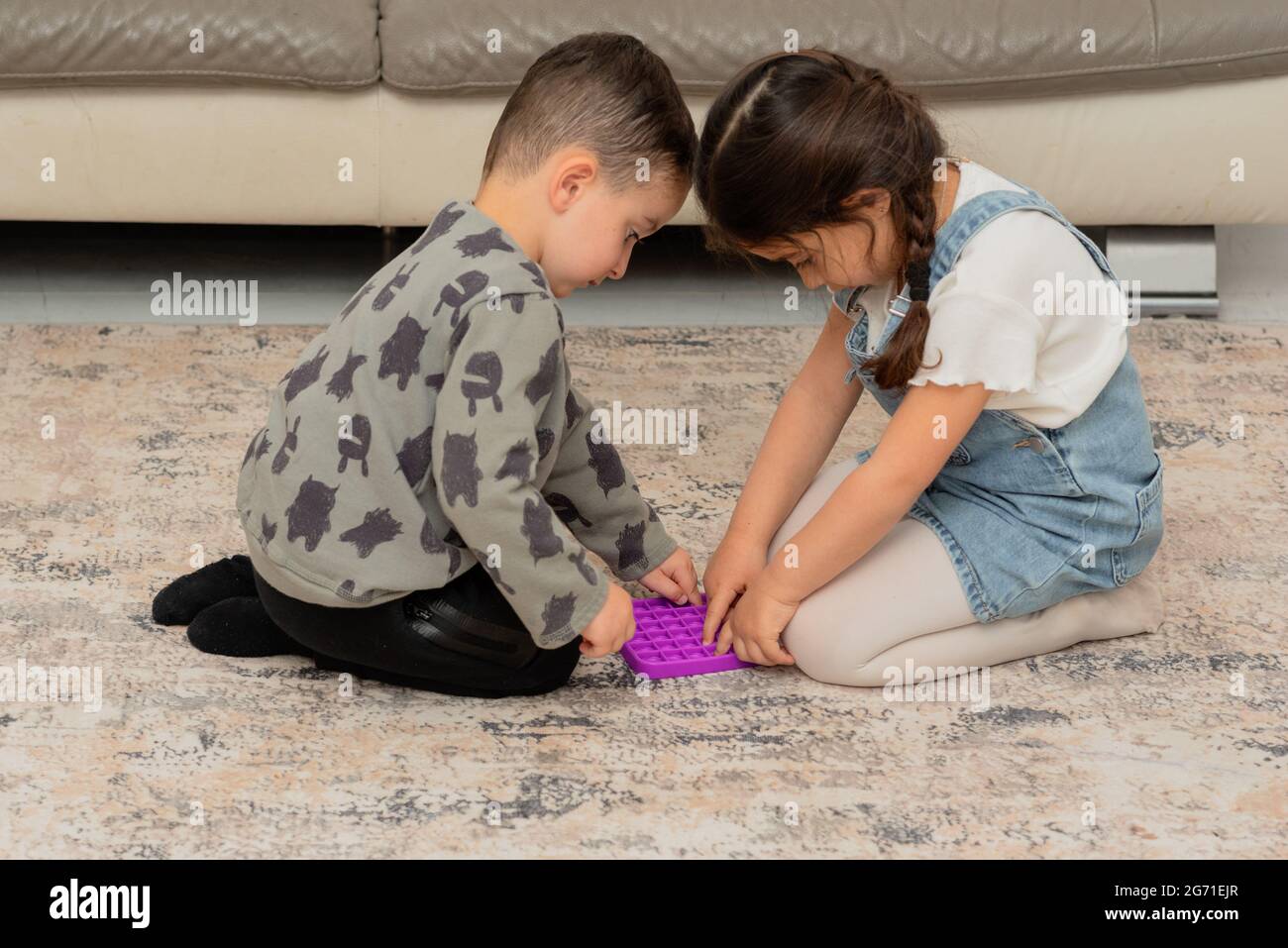Two cute funny children playing with the Pop It fidget. Happy family having fun together at home. Stock Photo