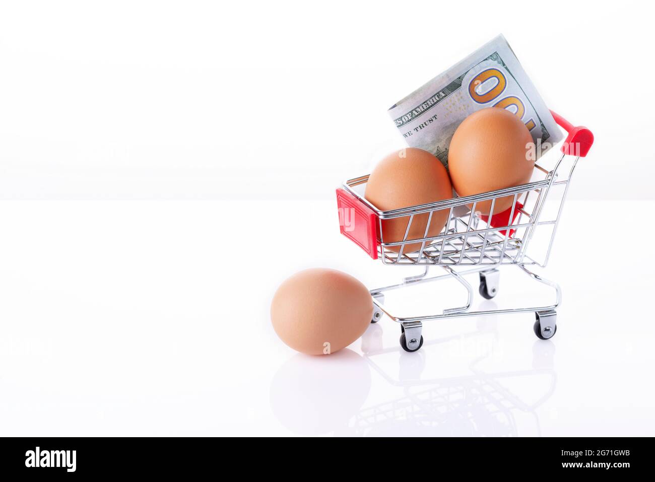 Eggs and 100 US  dollars in the shopping cart isolaten in white. Brown eggs in the basket. Copy space Stock Photo