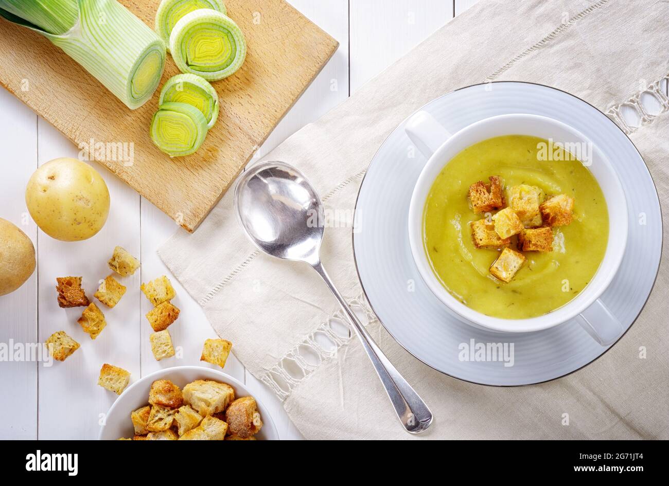 Leek and potato soup with croutons. Tasty and healthy homemade vegetable soup, served on a white wooden table with an embroidered linen tablecloth. To Stock Photo