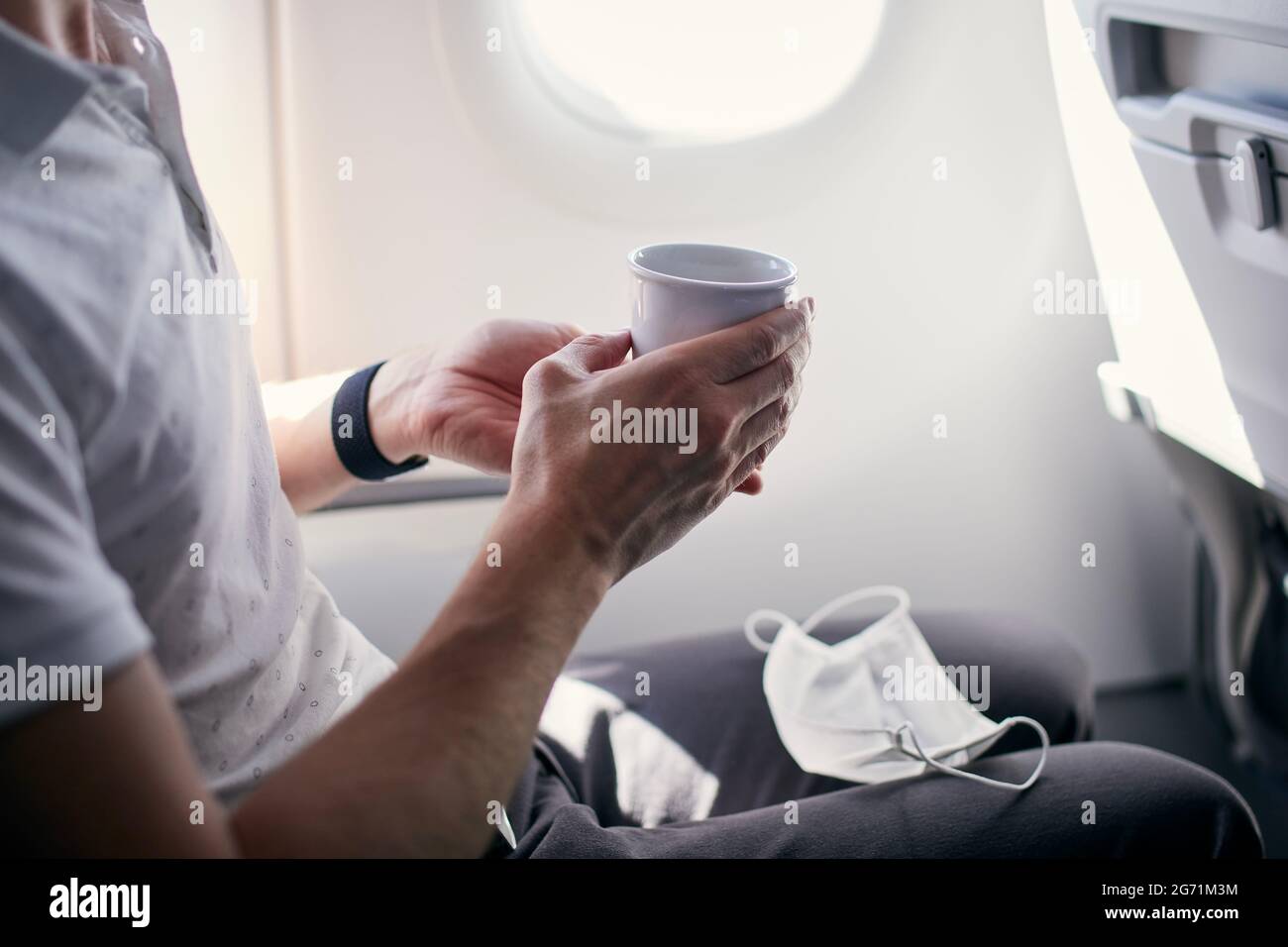 Passenger with face mask drinking coffee in airplane. Themes traveling during pandemic covid-19. Stock Photo