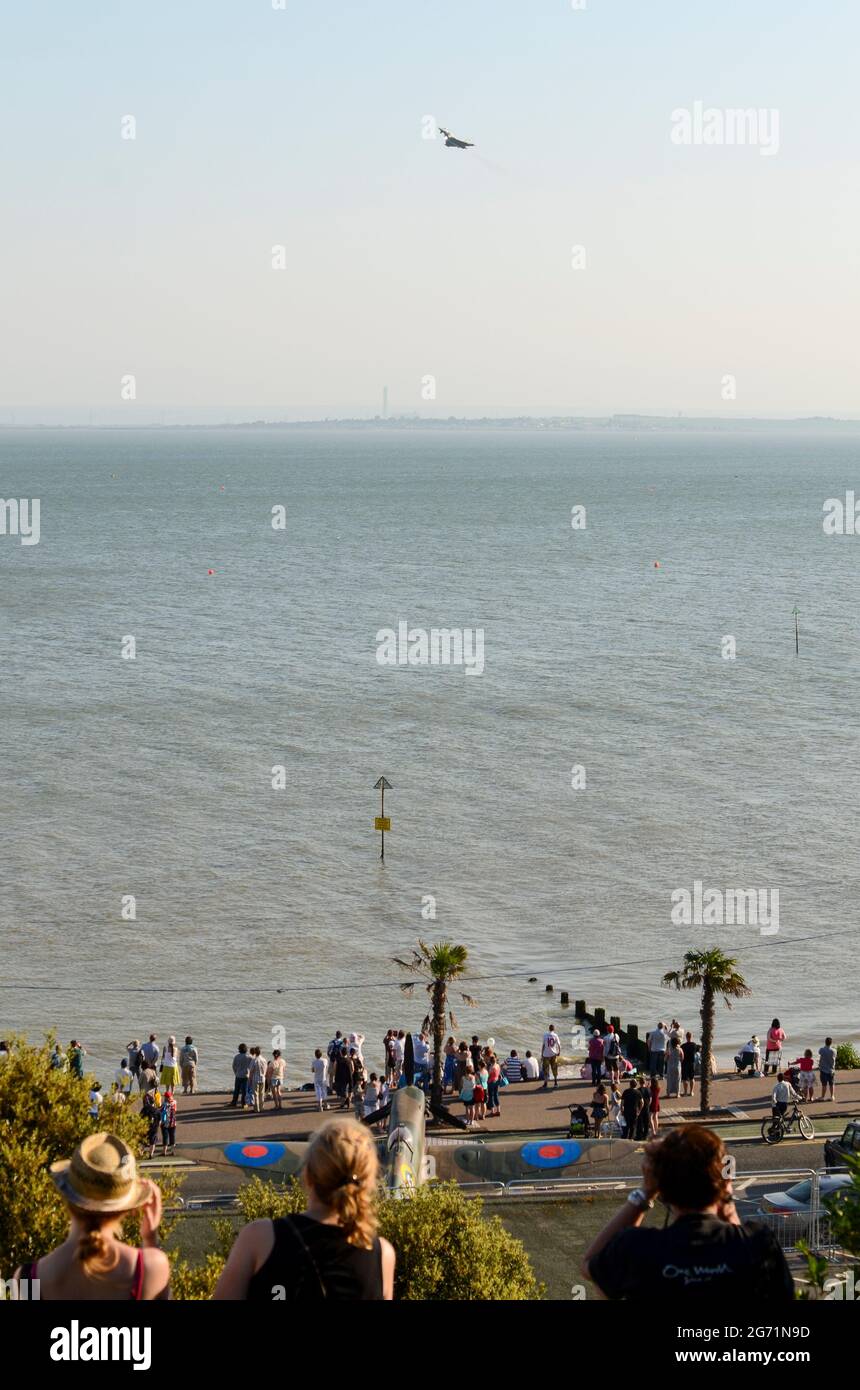 Southend Airshow 2012. Seafront crowds with displaying aircraft flying over the Thames Estuary. RAF Typhoon fighter jet climbing. WWII Spitfire below Stock Photo