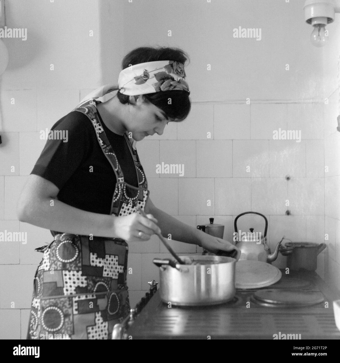 young pretty woman wearing apron cooking meal on an old style gas cooker 1960s hungary Stock Photo