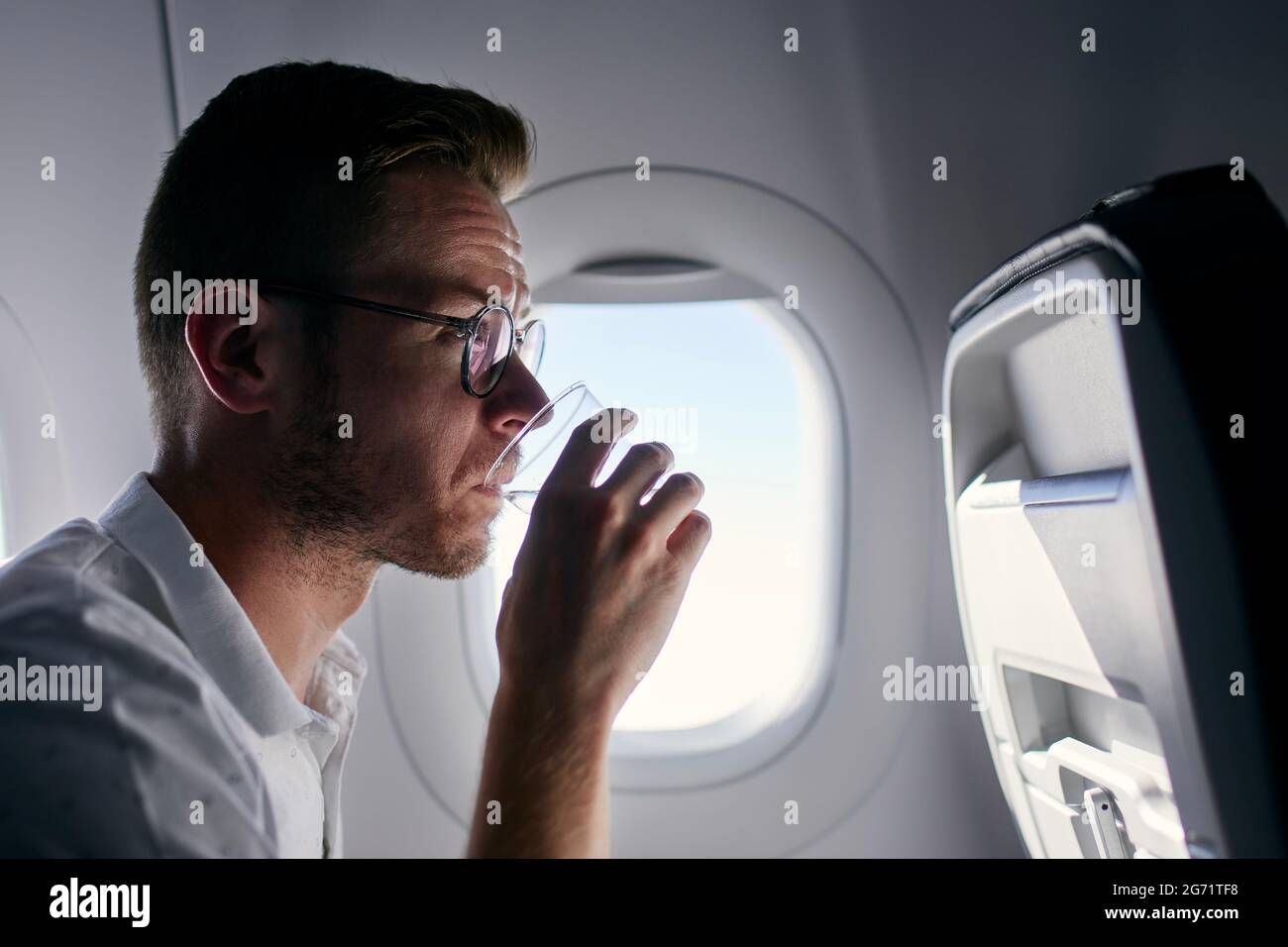 Portrait of passenger during flight. Young man drinking water from plastic cup. Stock Photo