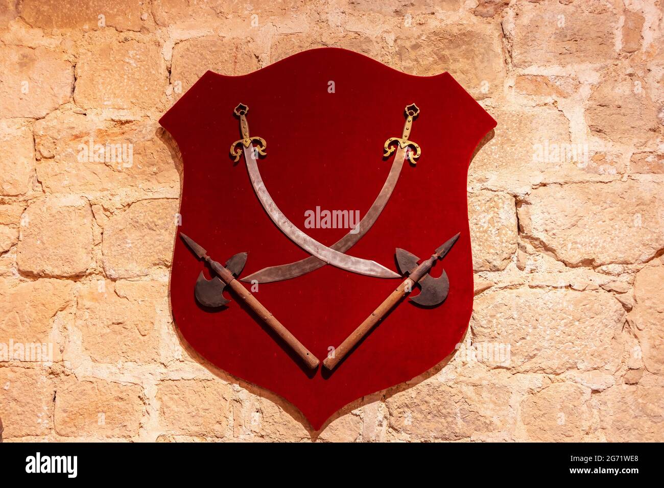 Swords and axes hung on the wall on a red velvet shield Stock Photo