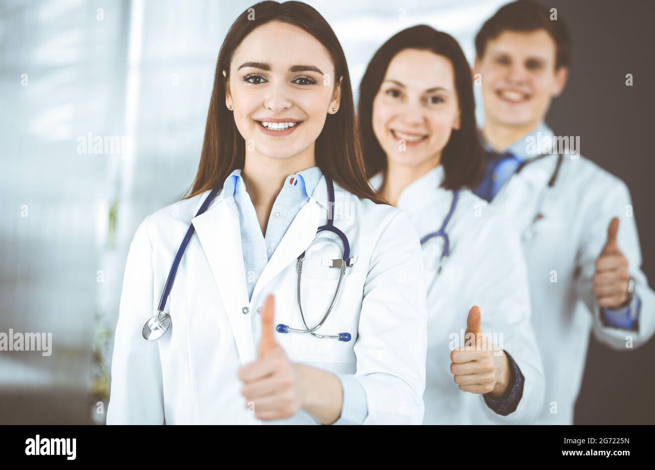 Group of young cheerful doctors is standing as a team with thumbs up in ...