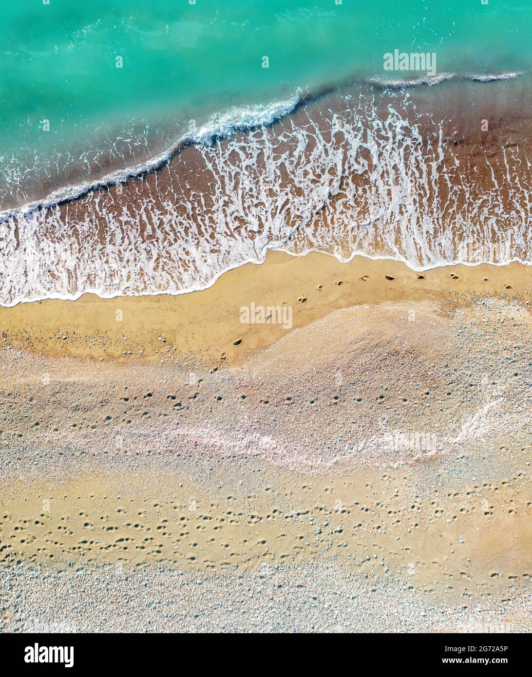 Human and dog footprints on a sandy shore along the sea with breaking waves, aerial vertical shot directly above Stock Photo