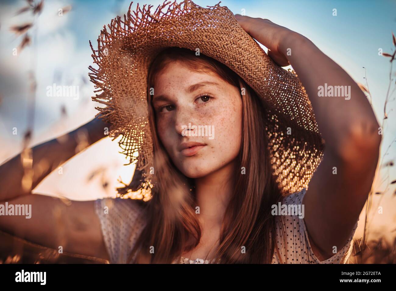Portrait of young, teen, ginger girl with freckles in the wheat field wearing a summer hat Stock Photo