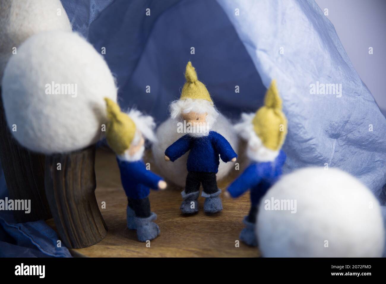 Three knitted fictional characters - dwarves dressed in blue by fluffy white balls in the scene Stock Photo