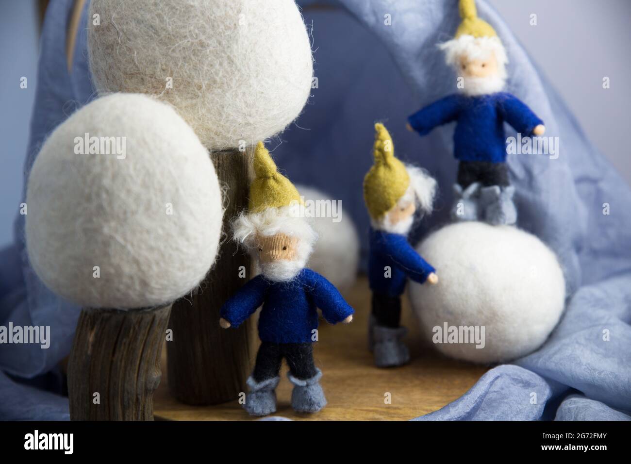 Three knitted fictional characters - dwarves dressed in blue by fluffy white balls in the scene Stock Photo