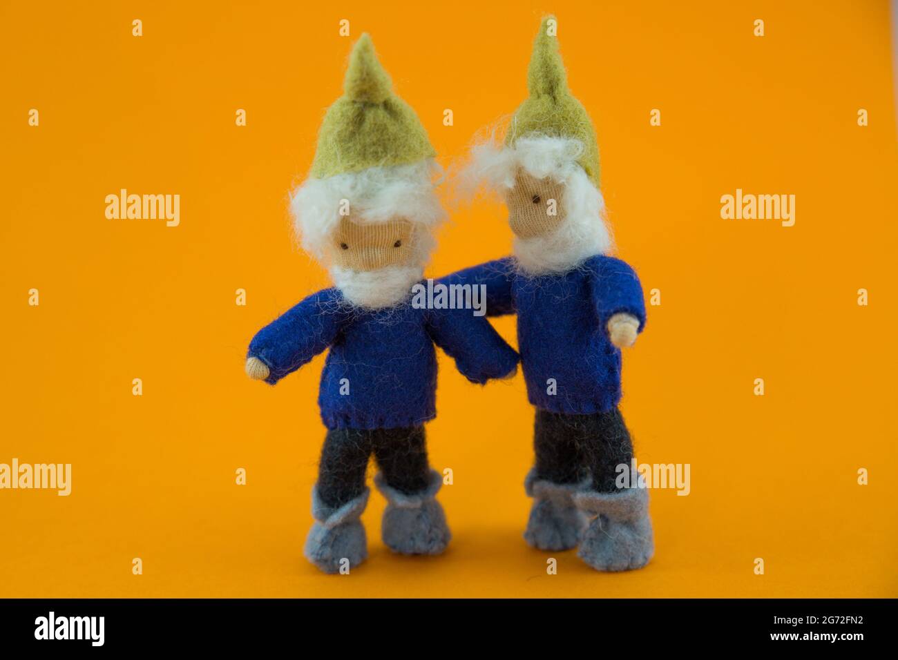 Two knitted fictional characters - dwarves dressed in blue with a bright orange background Stock Photo