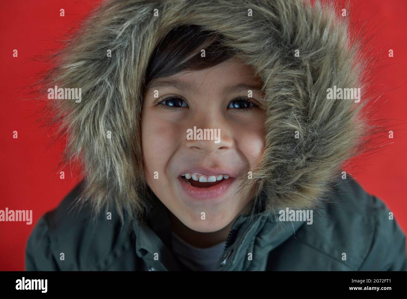 Funny cute adorable brunette smiling boy in green overcoat parka against  red background. horizontal Stock Photo - Alamy