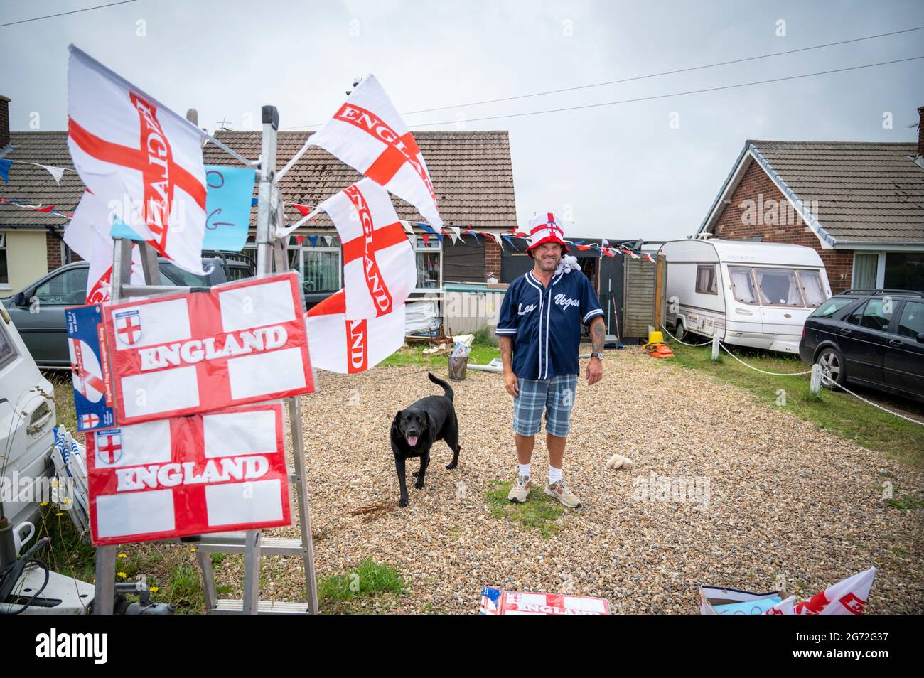 Trimingham, North Norfolk, UK. 10th July, 2021. A man sells England football flags, hats, signs and other supporters souvenirs from his driveway ahead of the England V Italy European Football Championships final at Wembley. Credit: Julian Eales/Alamy Live News Stock Photo