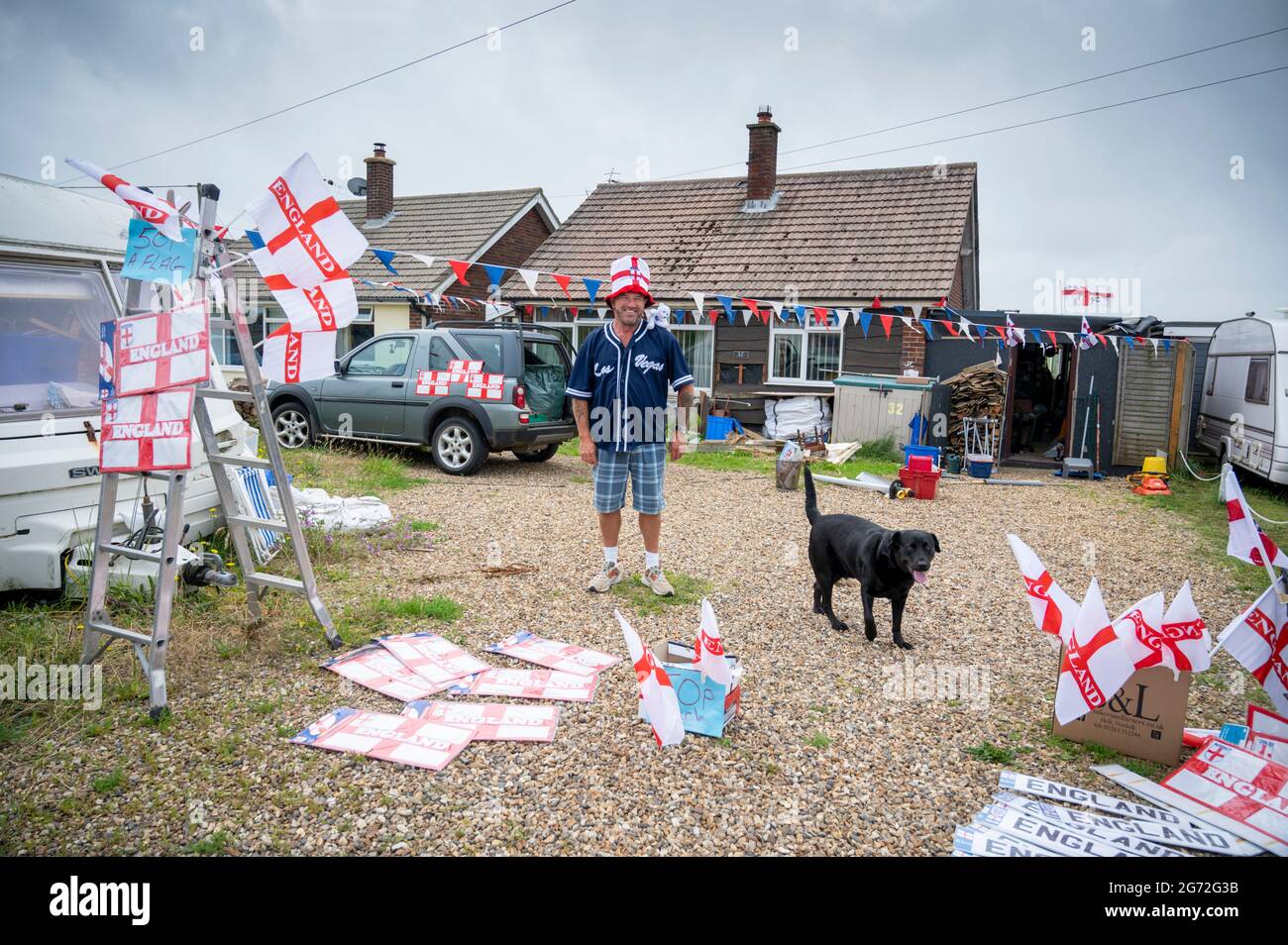 Trimingham, North Norfolk, UK. 10th July, 2021. A man sells England football flags, hats, signs and other supporters souvenirs from his driveway ahead of the England V Italy European Football Championships final at Wembley. Credit: Julian Eales/Alamy Live News Stock Photo